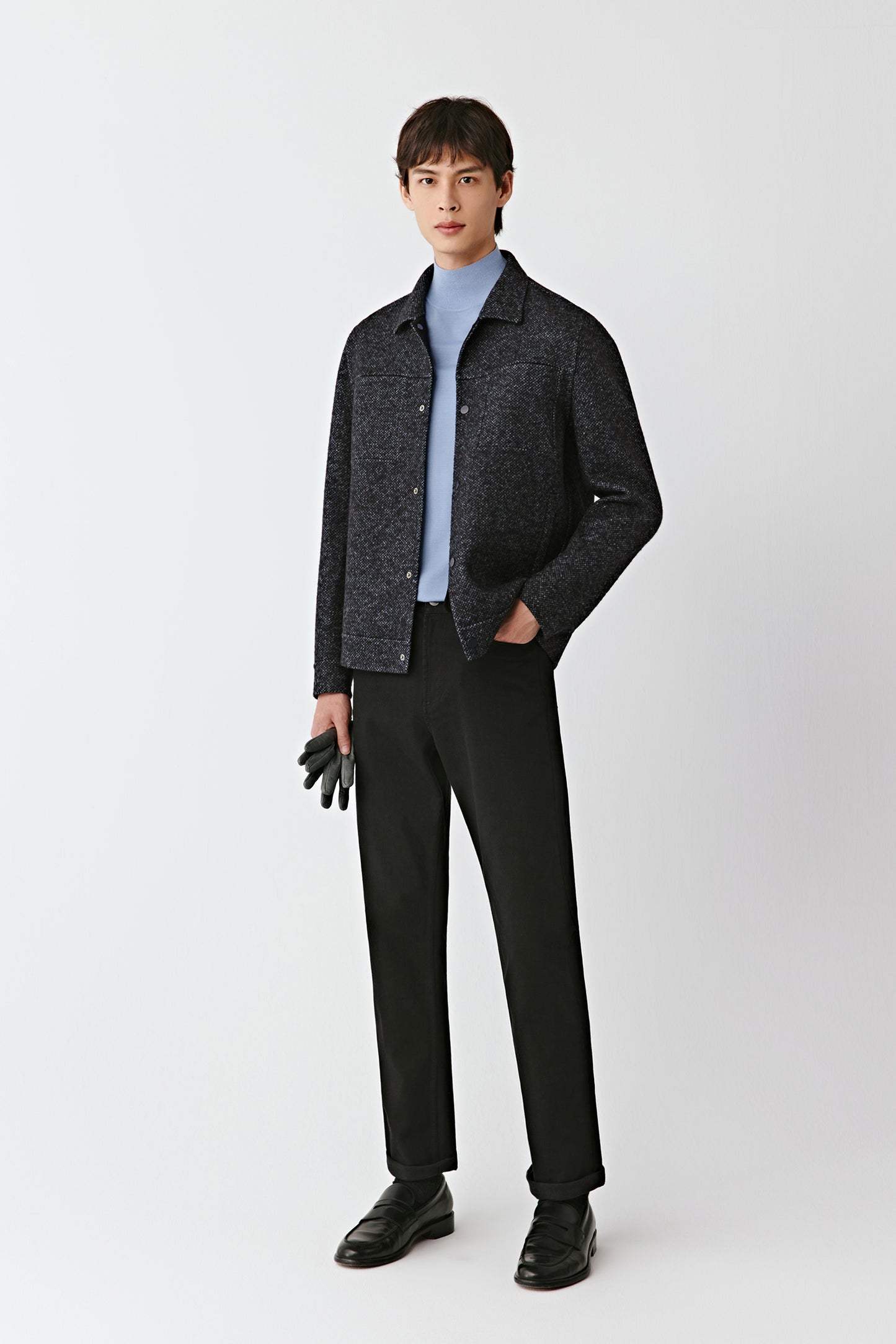 Man wearing a dark jacket, light shirt, and black pants on a white background