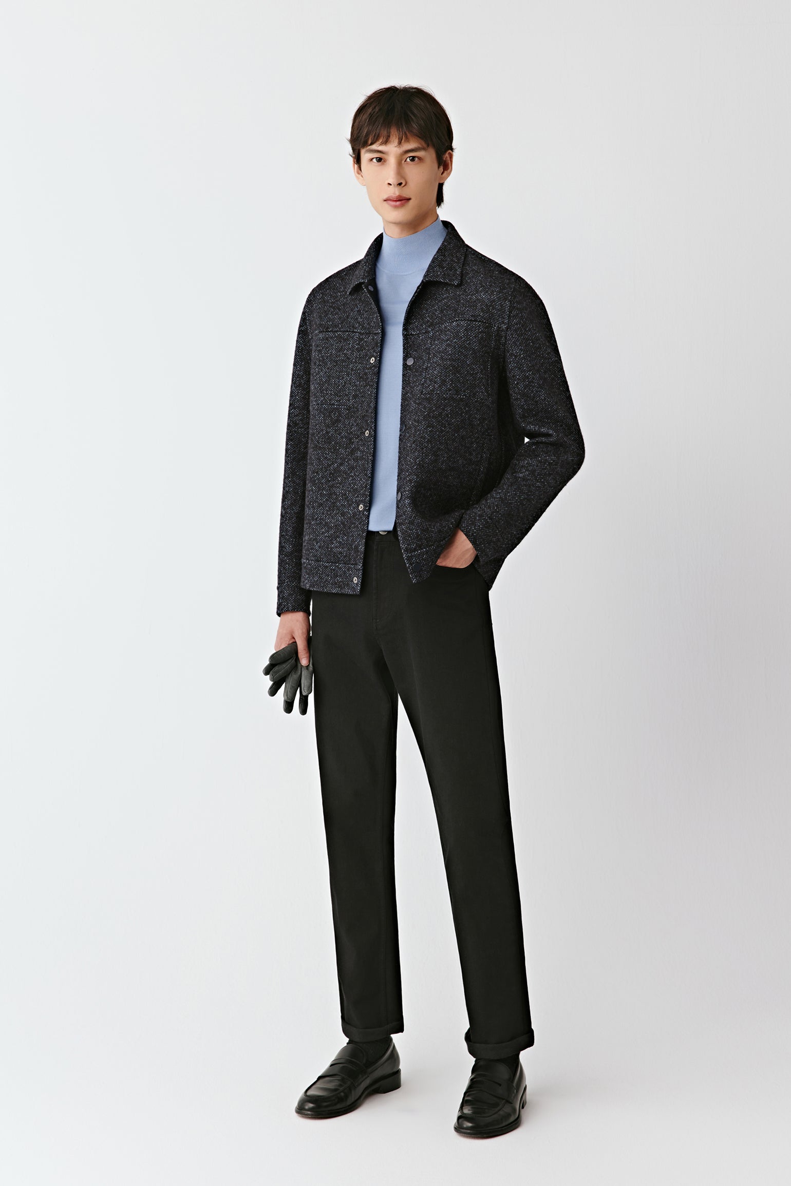 Man wearing a dark jacket, light shirt, and black pants on a white background