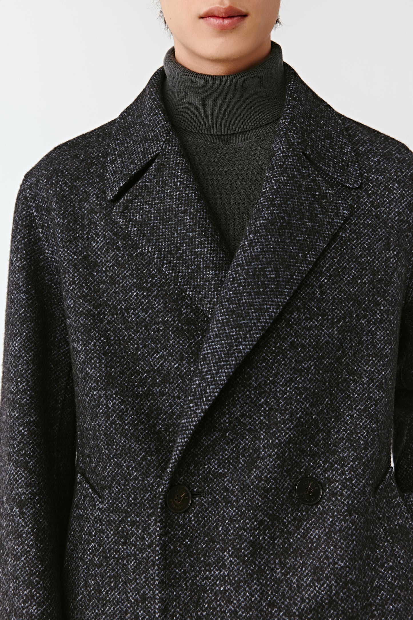 Close-up of a person wearing a dark gray textured coat with a plain background