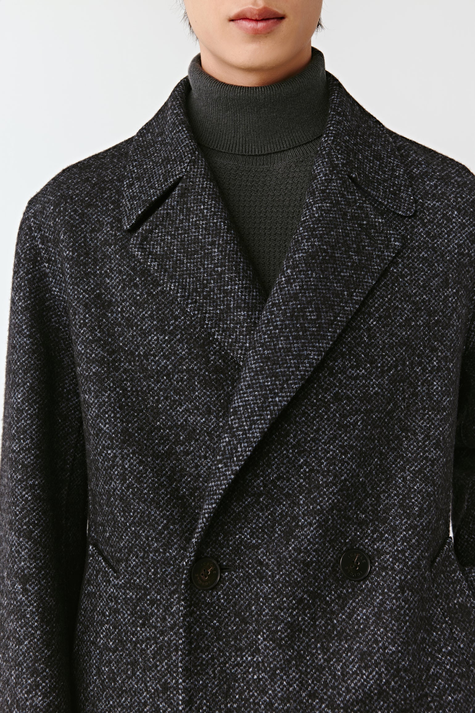 Close-up of a person wearing a dark gray textured coat with a plain background