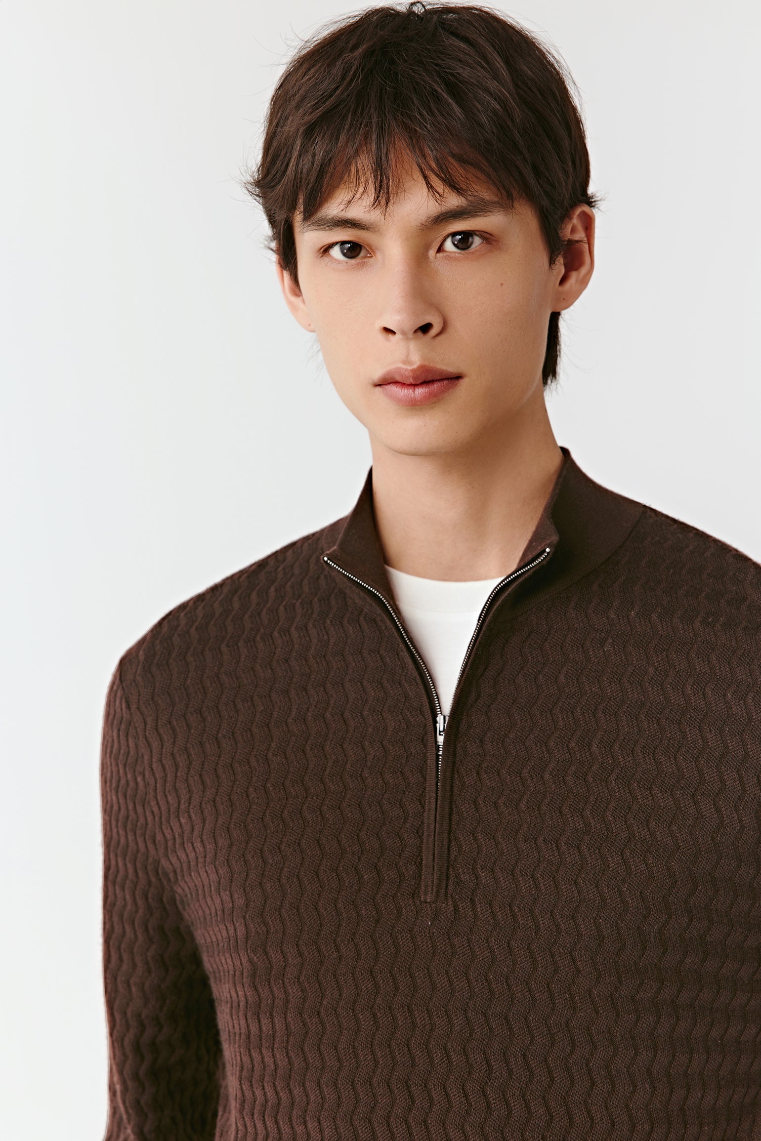Man wearing a brown textured sweater over a white shirt on a light gray background