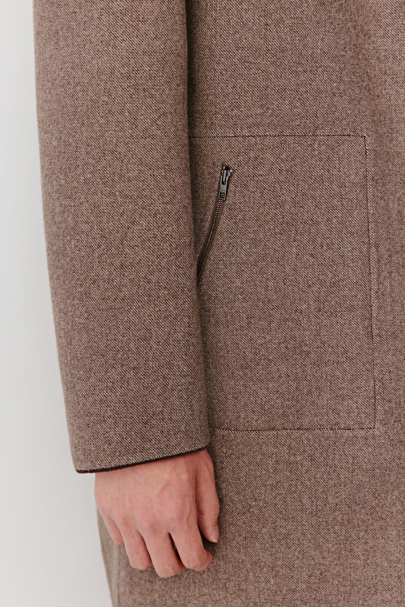 Close-up of a brown coat with a hand partially visible, on a white background