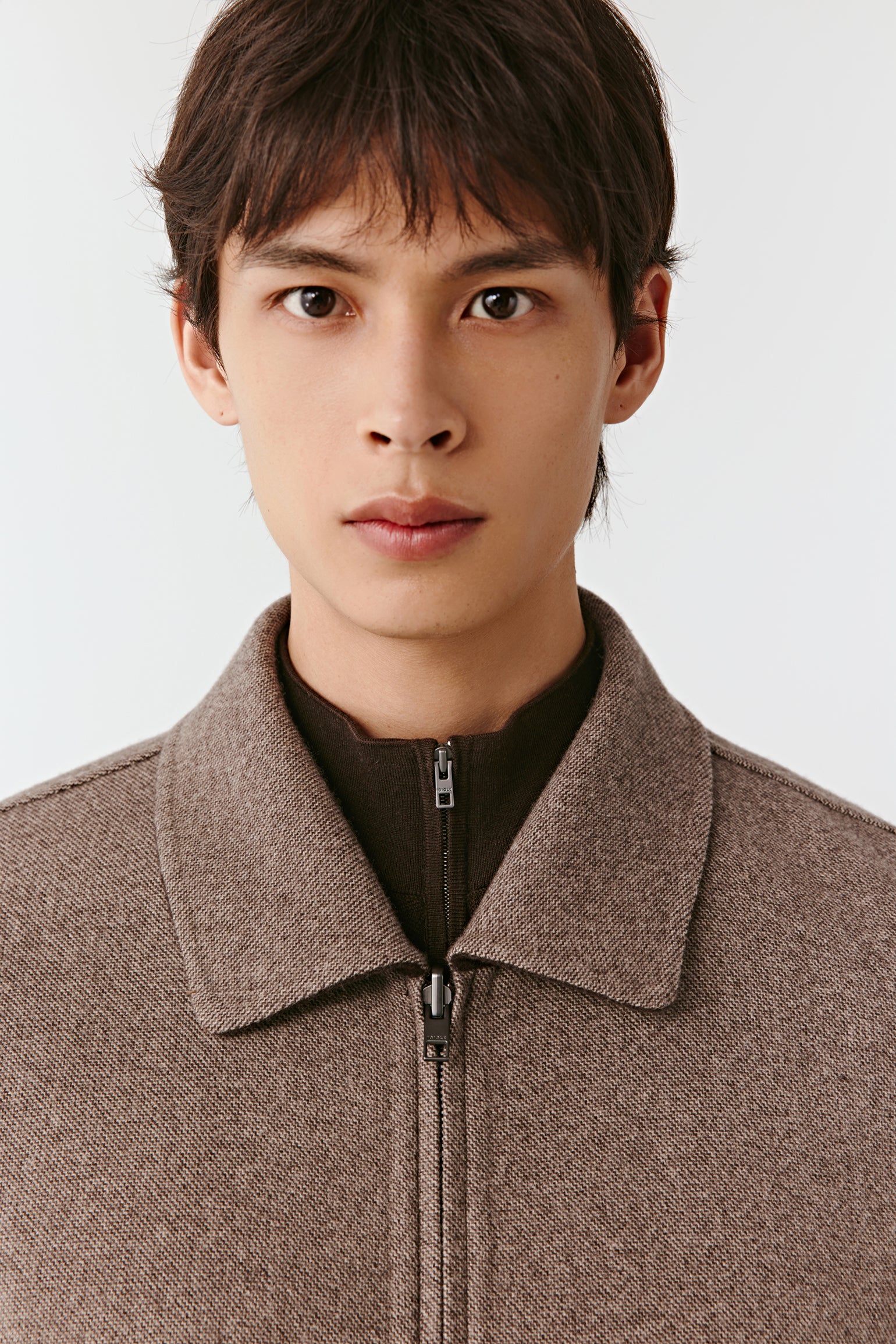 Person wearing a brown jacket with a plain background