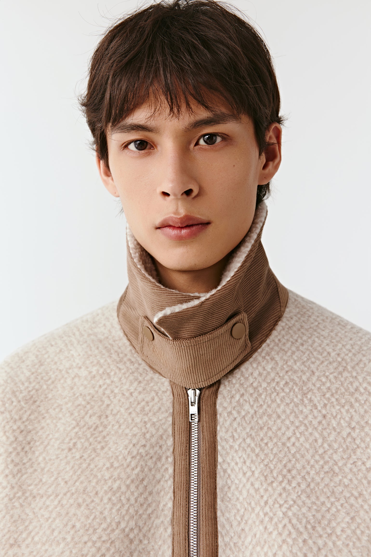 Person wearing a beige jacket with a high collar and zipper on a white background