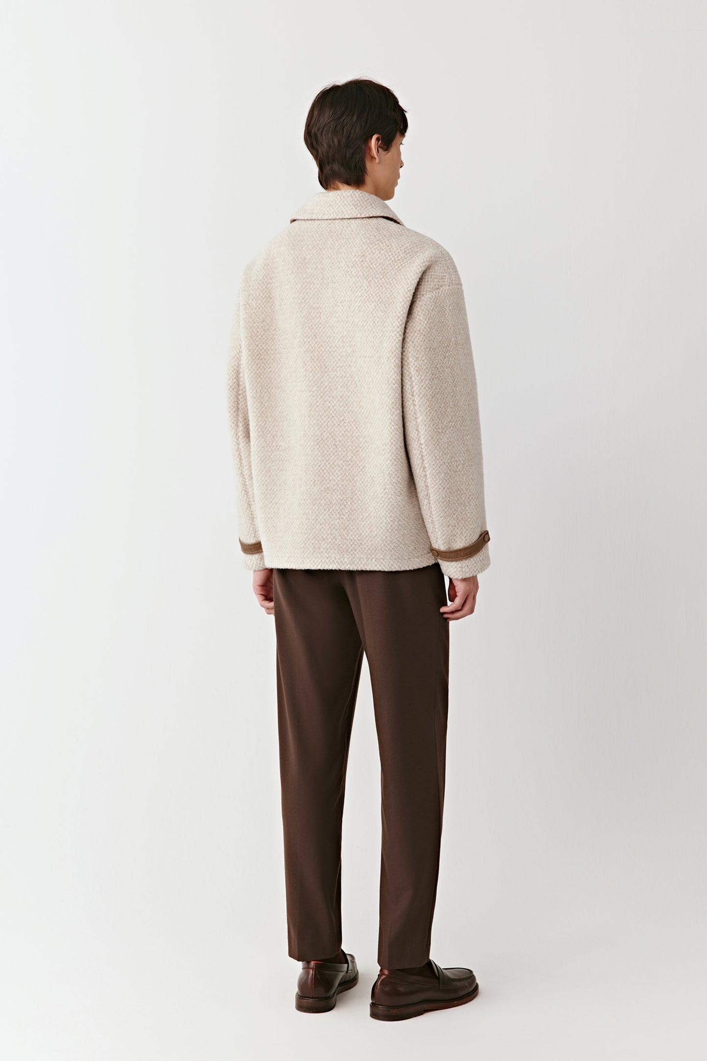 Person wearing a beige jacket and brown pants on a white background