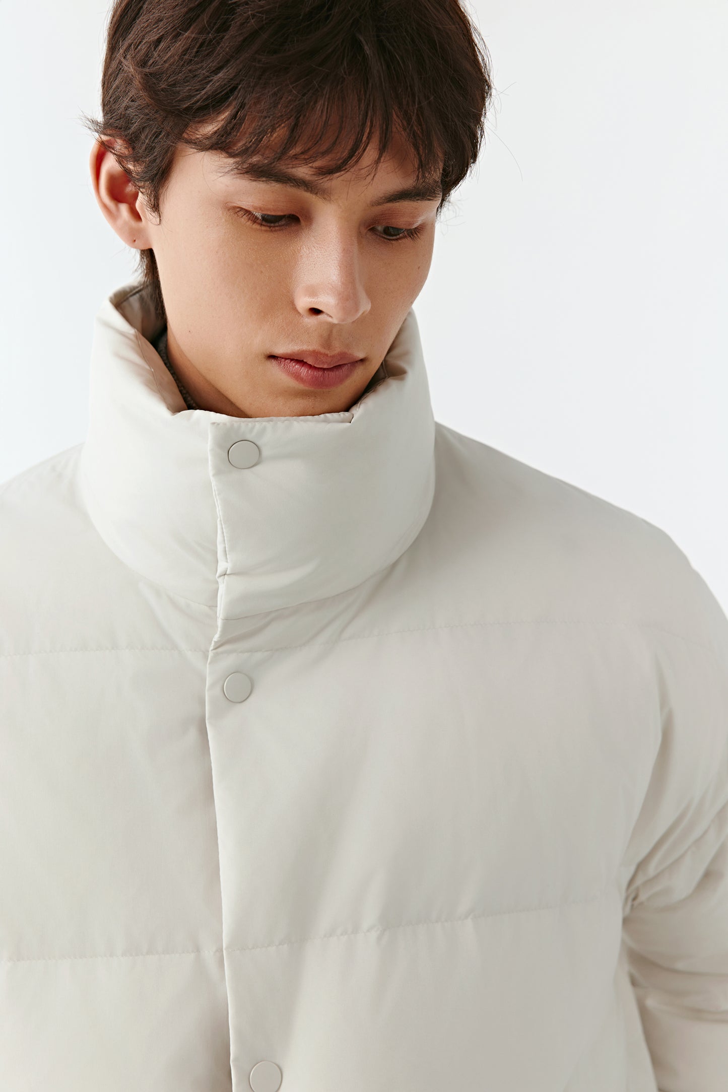 Close-up of the high stand collar of the cream puffer coat, showing the padded construction and smooth fabric.