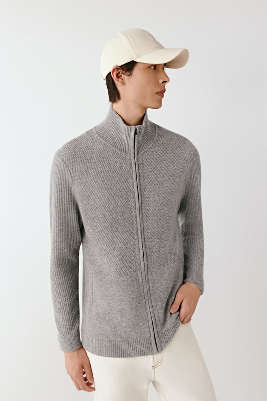 Person wearing a gray zip-up sweater and white cap on a light background