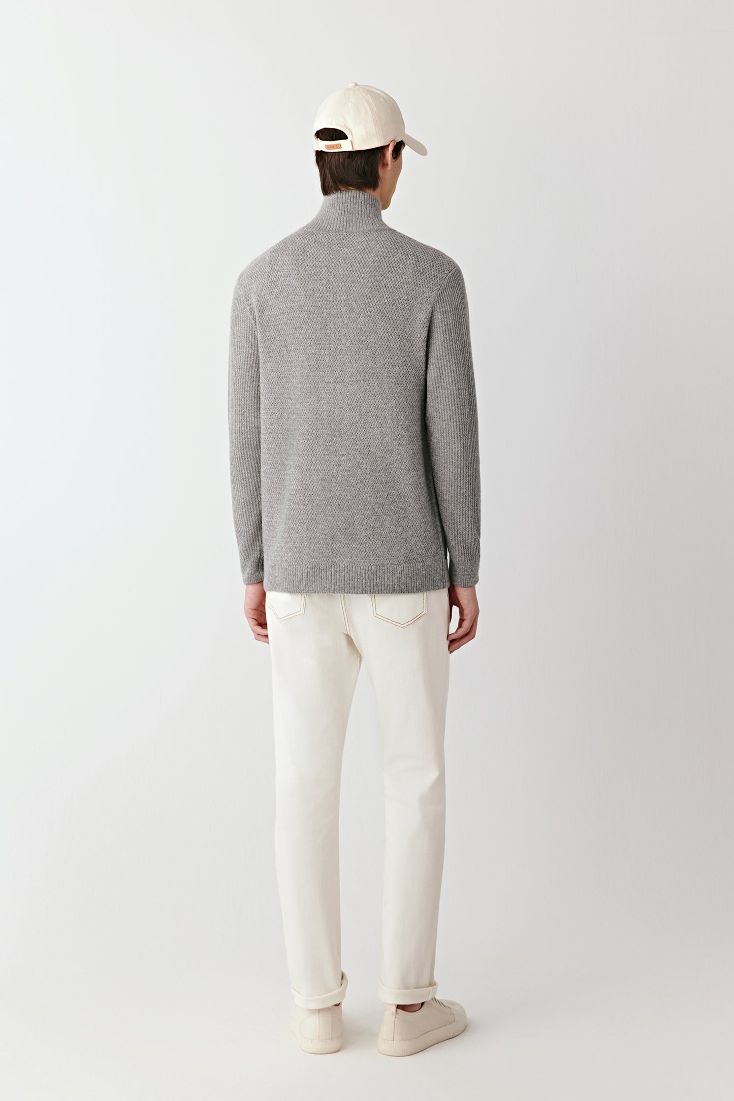 Person wearing a gray sweater and white pants on a plain background