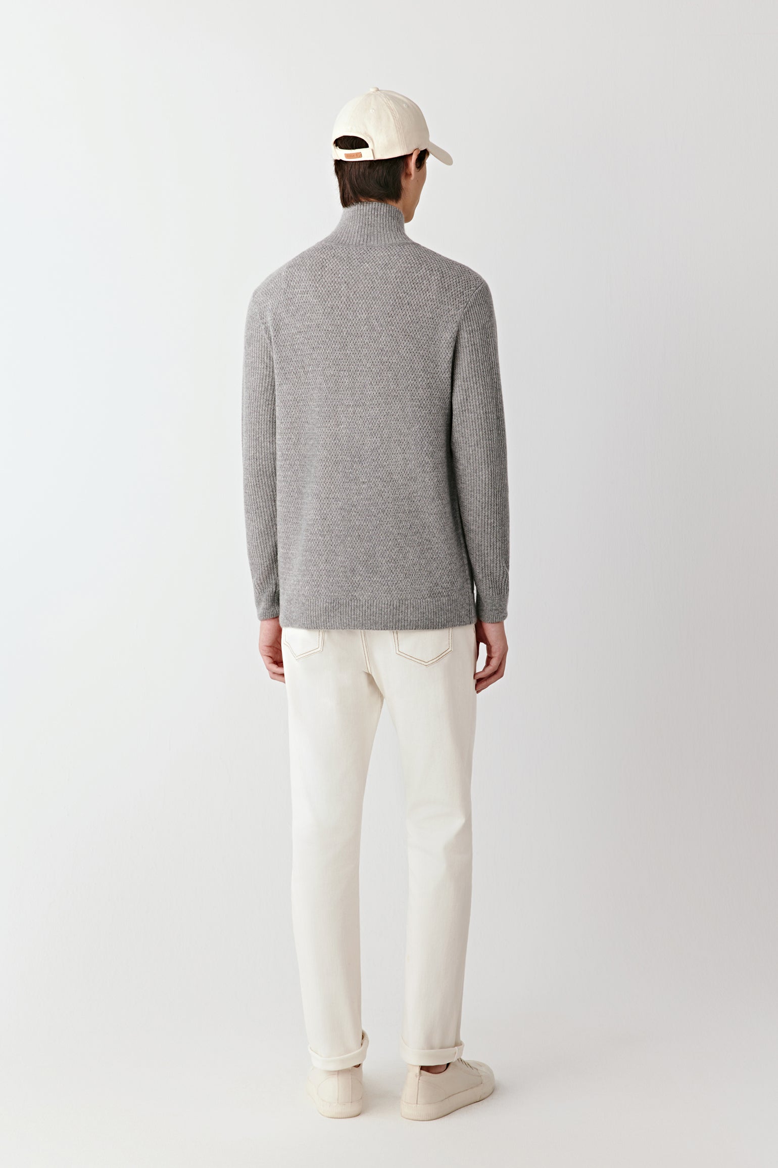 Person wearing a gray sweater and white pants on a plain background