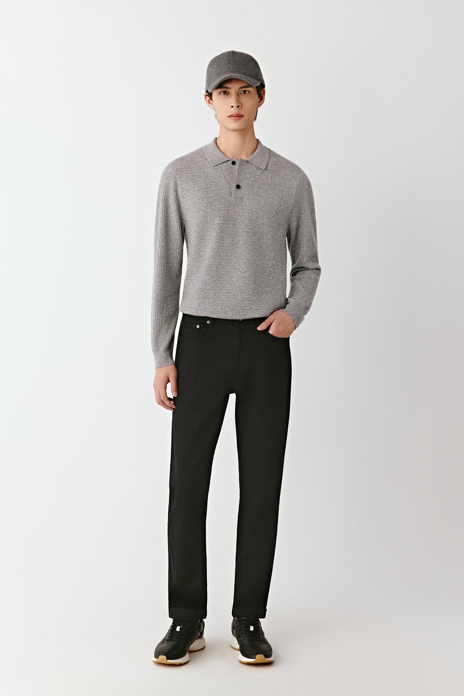 Person wearing a gray long-sleeve polo shirt and black pants on a white background