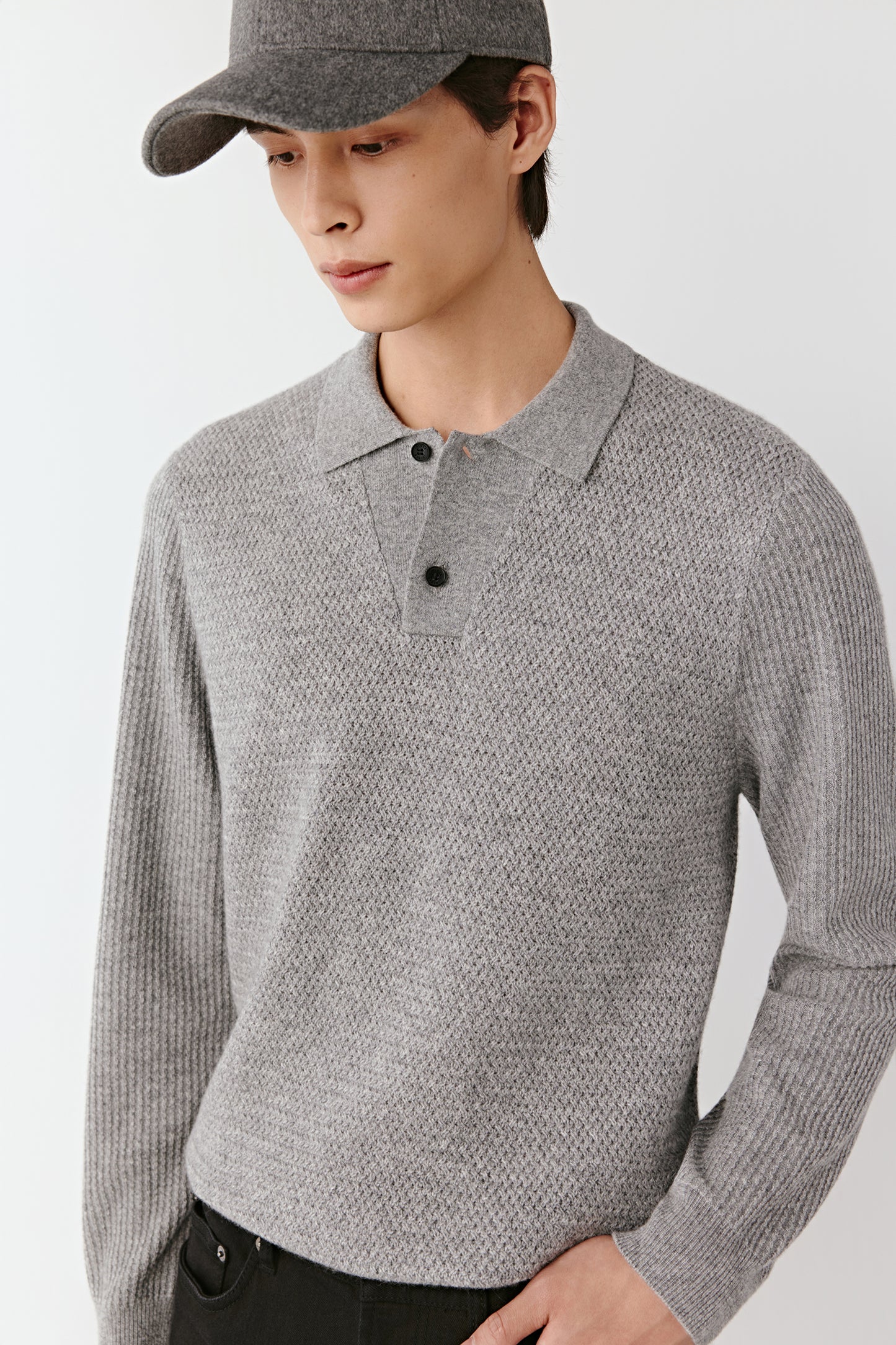 Person wearing a gray textured sweater and cap on a white background