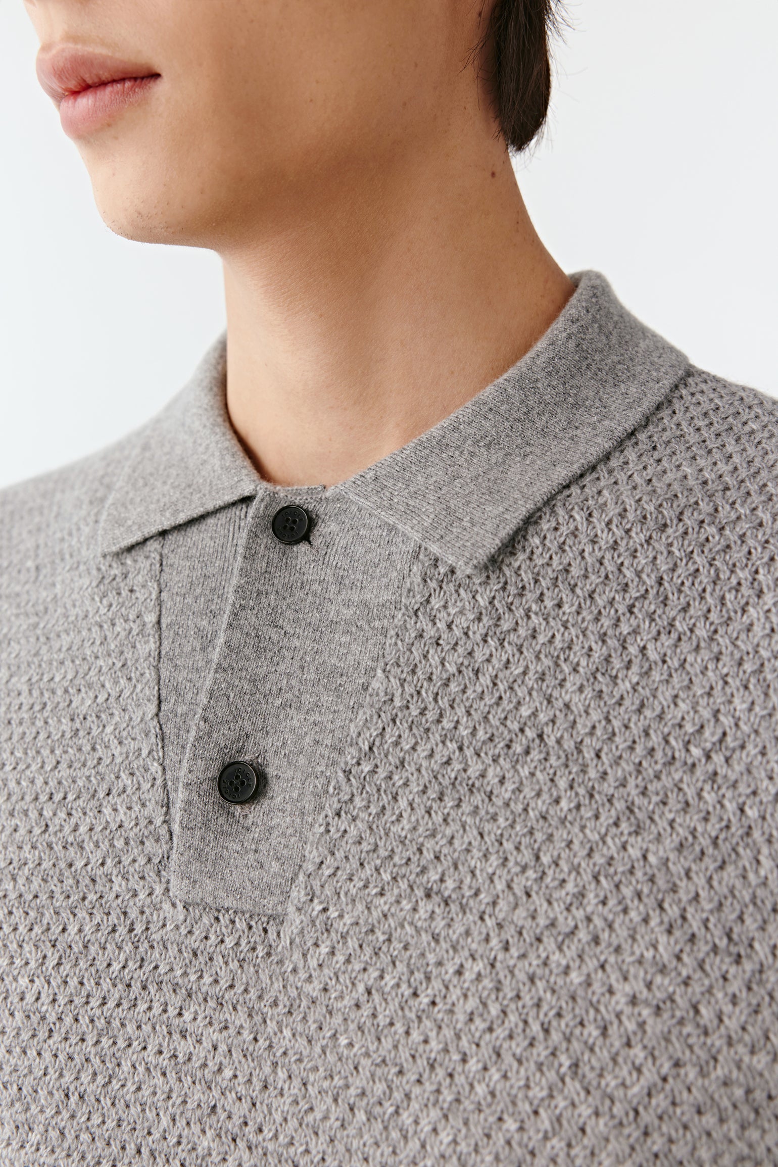 Close-up of a person wearing a textured gray sweater with black buttons on a plain background