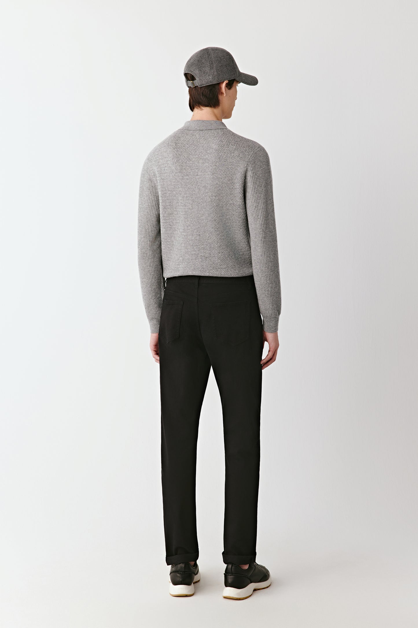 Person wearing a gray sweater and black pants on a white background