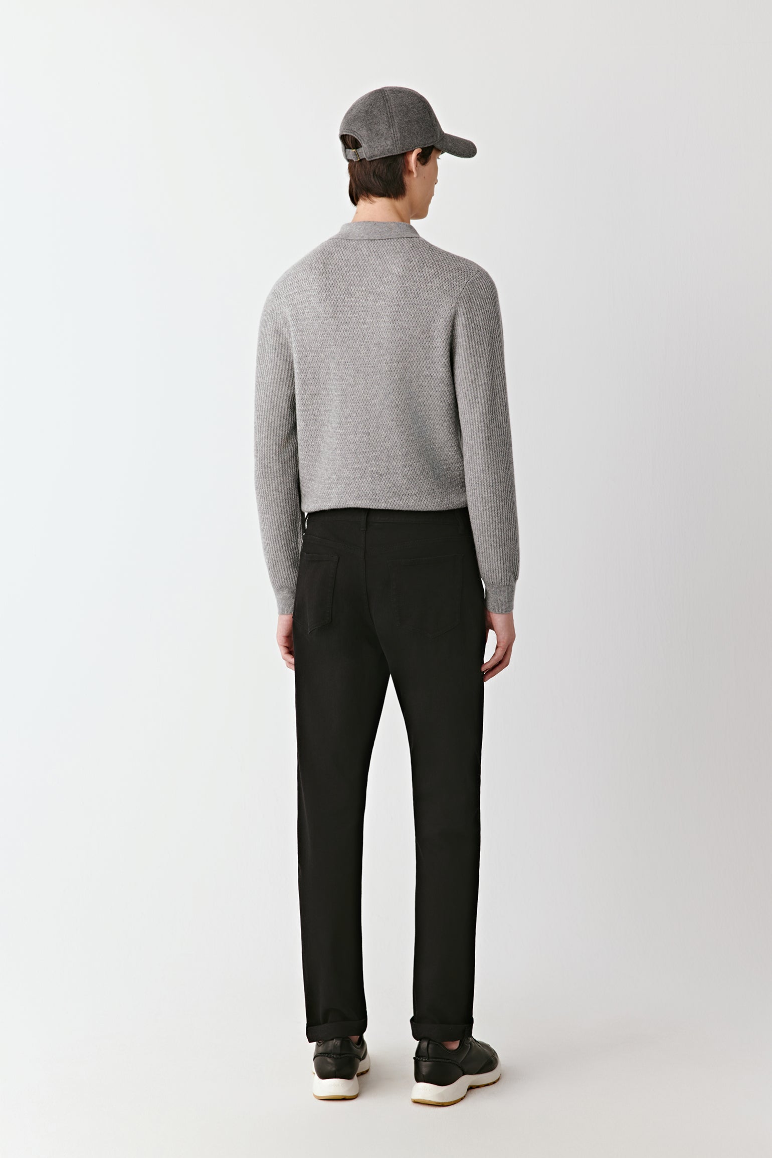 Person wearing a gray sweater and black pants on a white background