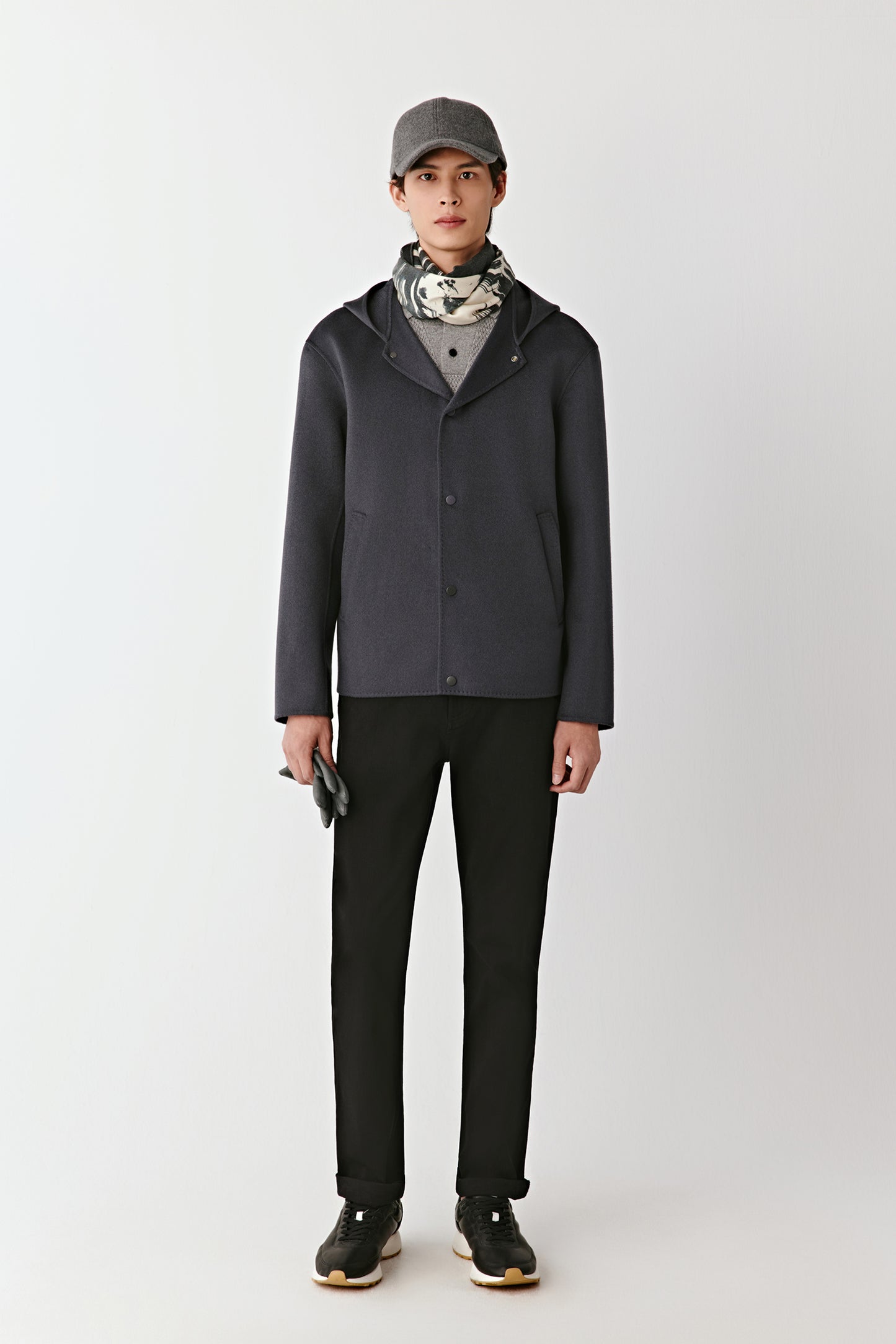 Person wearing a dark gray jacket, black pants, and a cap on a white background