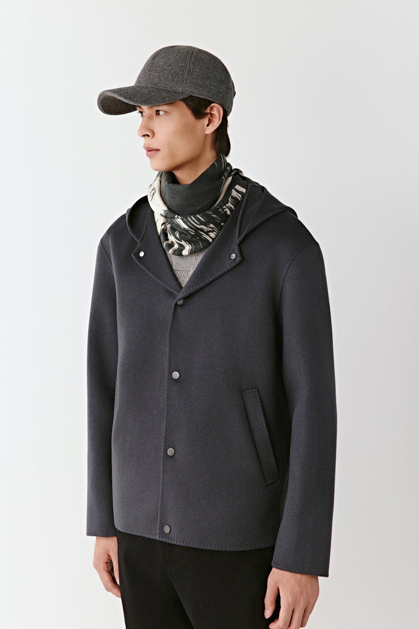 Person wearing a dark gray coat and cap on a white background