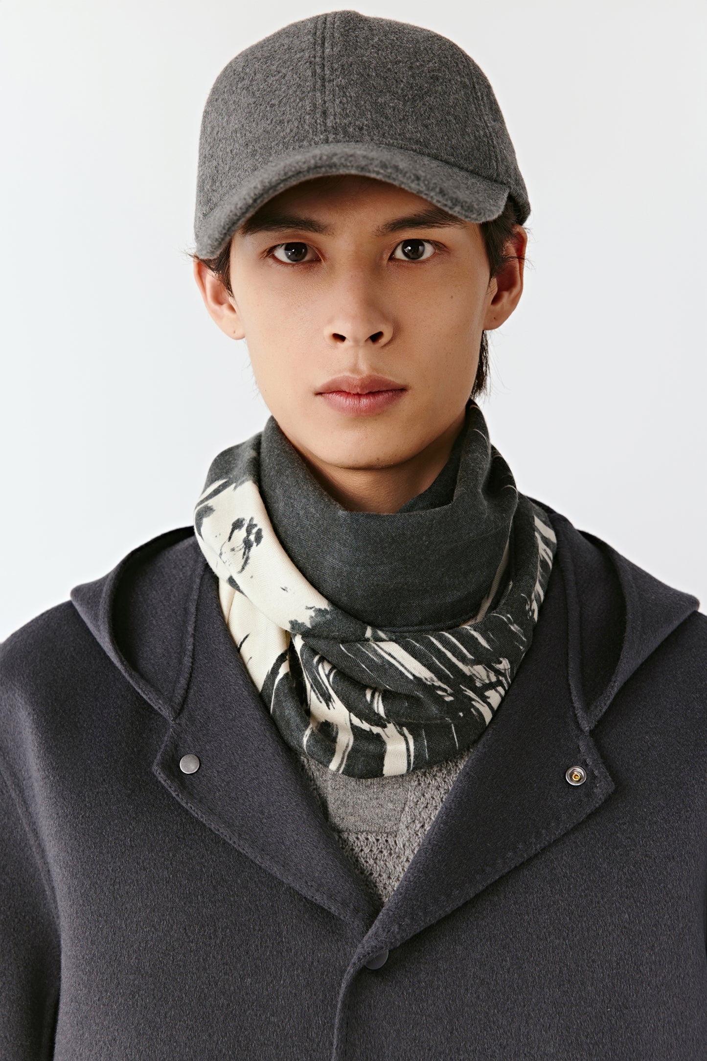 Men wearing a gray cap, dark coat, and patterned scarf on a white background