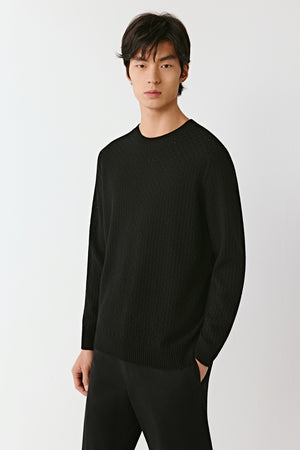 Man wearing a black wool and cashmere crewneck pullover with straight relaxed fit, styled with black trousers, front portrait view.