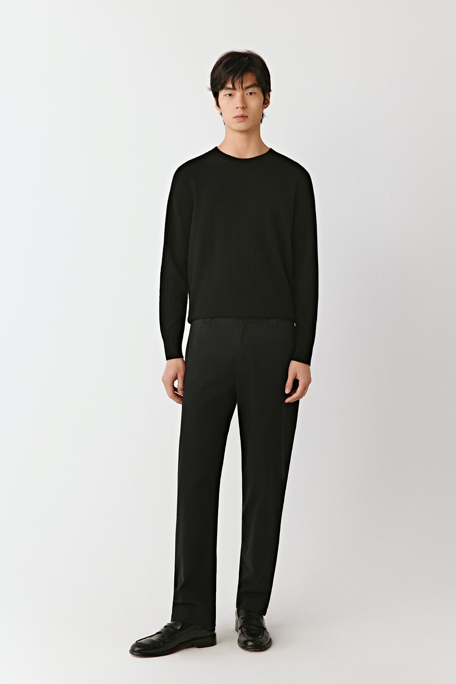 Full-length front view of a person wearing a black wool pullover with a crew neckline and clean, minimal lines.