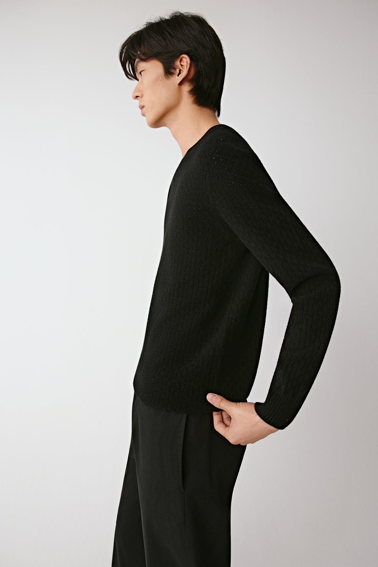 Side profile of the black wool pullover, highlighting the fluid silhouette and lightweight knit.