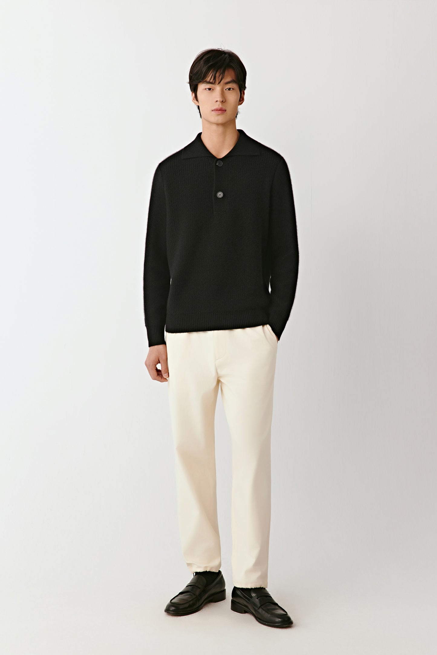 Full-length front view of a person wearing a black cashmere polo sweater with a buttoned placket and ribbed trims.