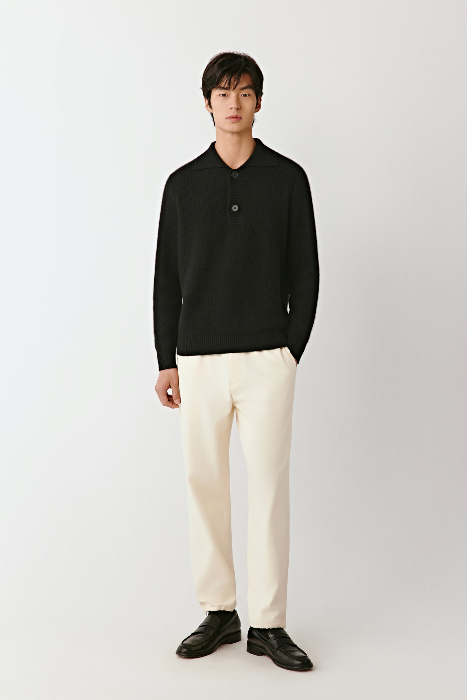 Full-length front view of a person wearing a black cashmere polo sweater with a buttoned placket and ribbed trims.