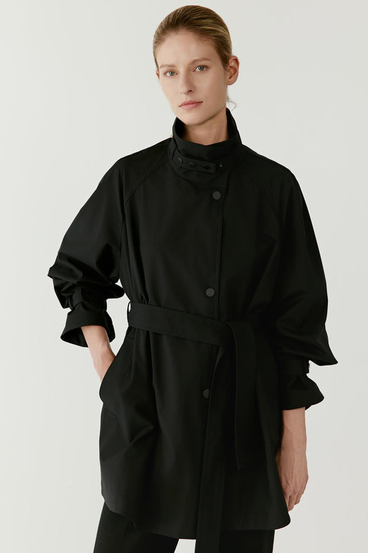 Front view of the short black trench coat showing the belt tied at the waist, the clean front construction, and the structured high collar framing the neckline.