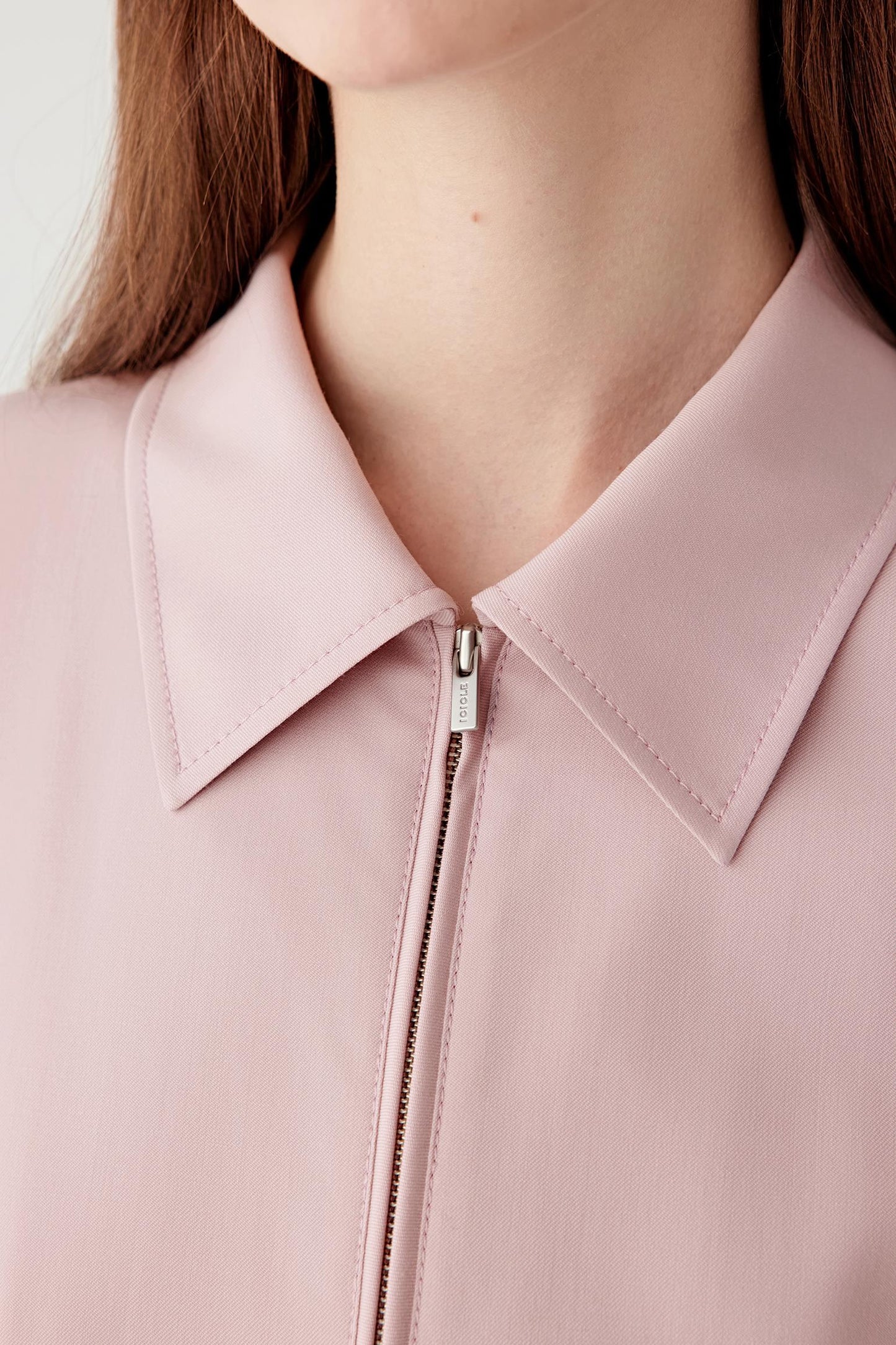 Close-up of the front neckline and zip fastening, revealing the fine wool twill weave and discreet metal zip.