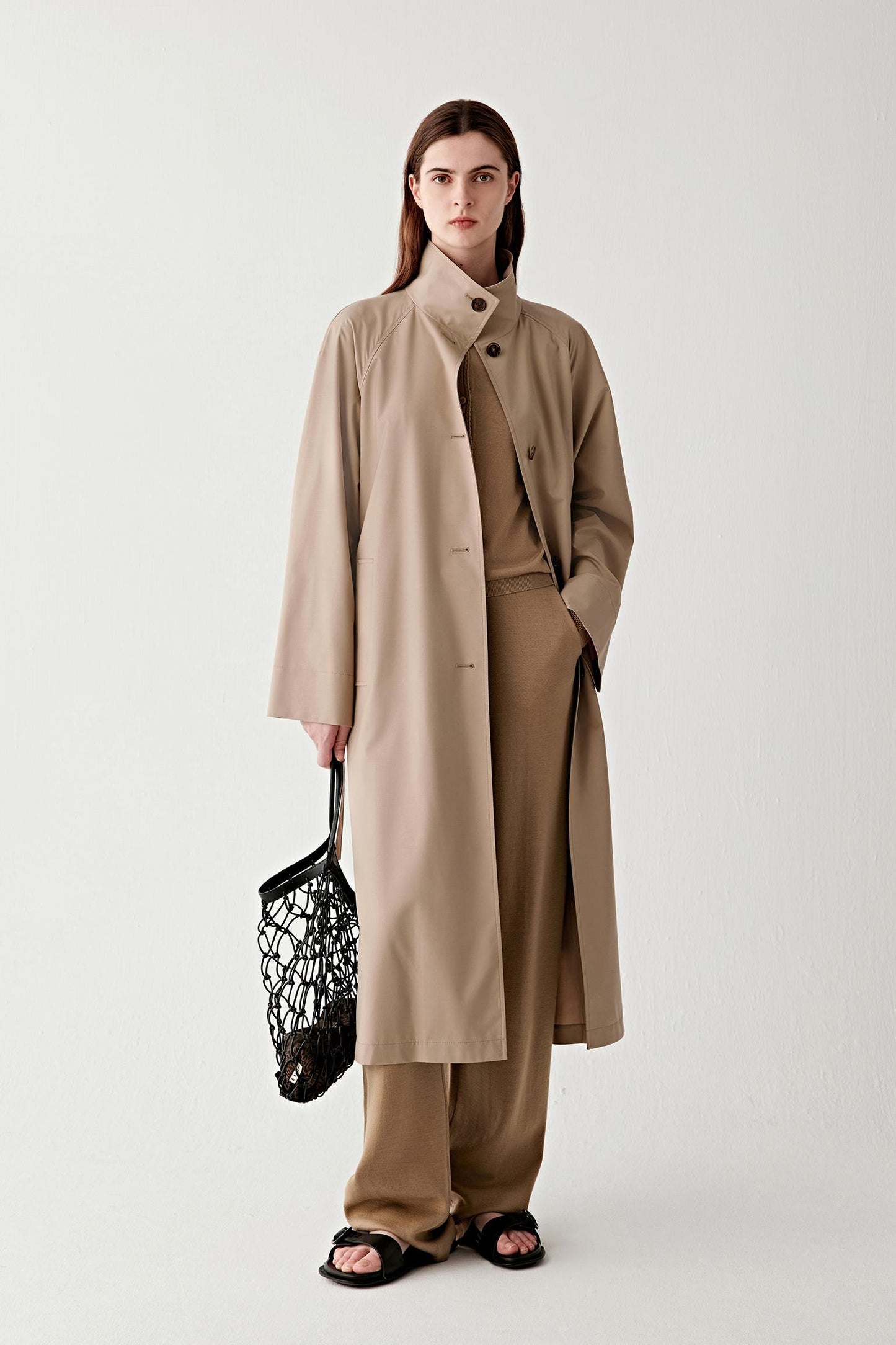 Full-length front view of a long camel trench coat in wool and silk, worn open to show its fluid drape and elongated silhouette.