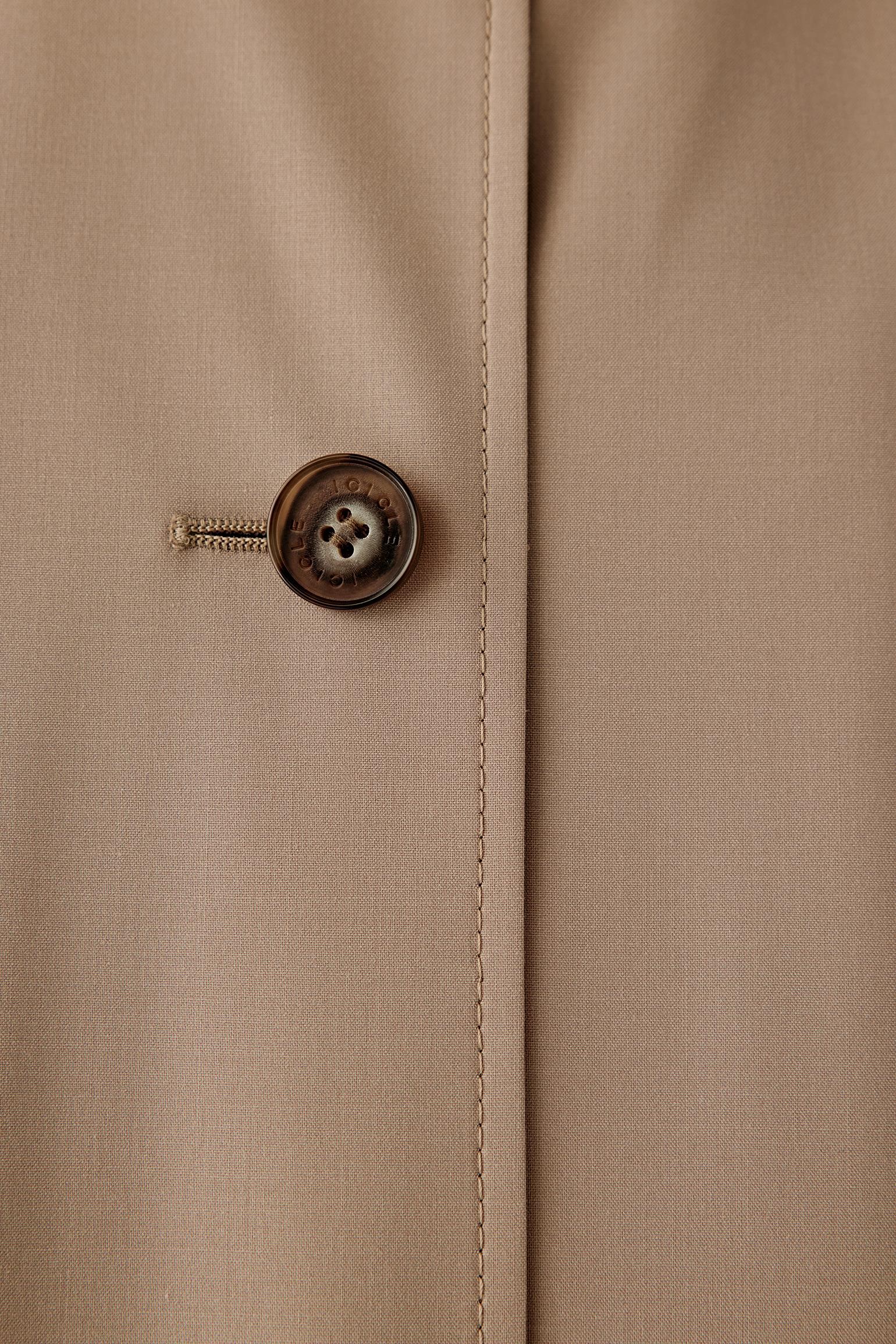 Close-up detail of the button fastening and fabric surface, showing refined finishing and tonal stitching.