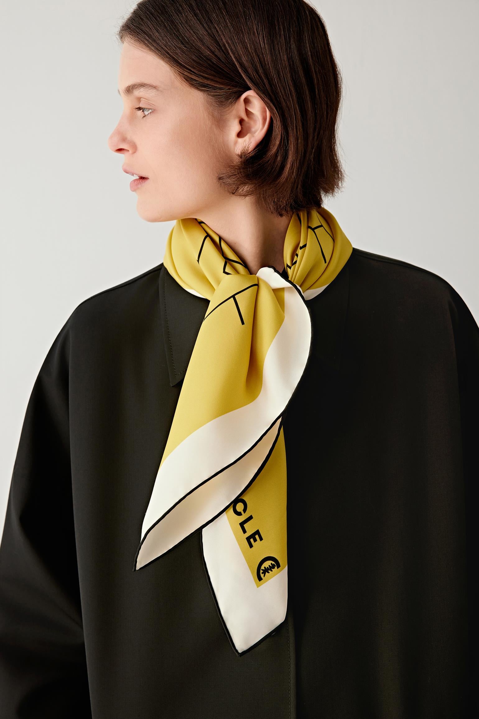 Woman wearing a yellow silk twill scarf tied at the neck with black geometric pattern.