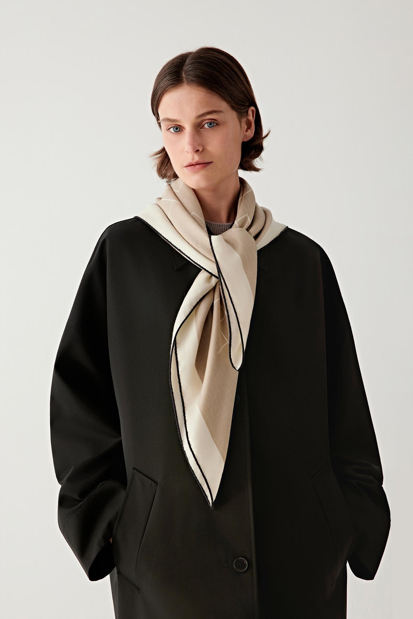 Woman wearing a beige cashmere and silk scarf tied at the neck over a black top.
