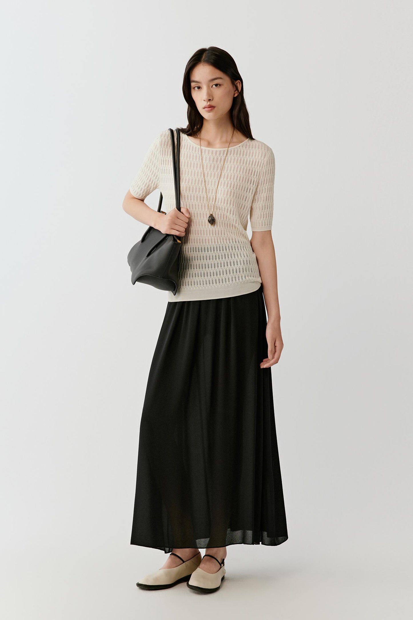 Full-length view highlighting the contrast between the lightweight cream knit top and the fluid black skirt, with the top falling straight at the waist and allowing ease of movement.