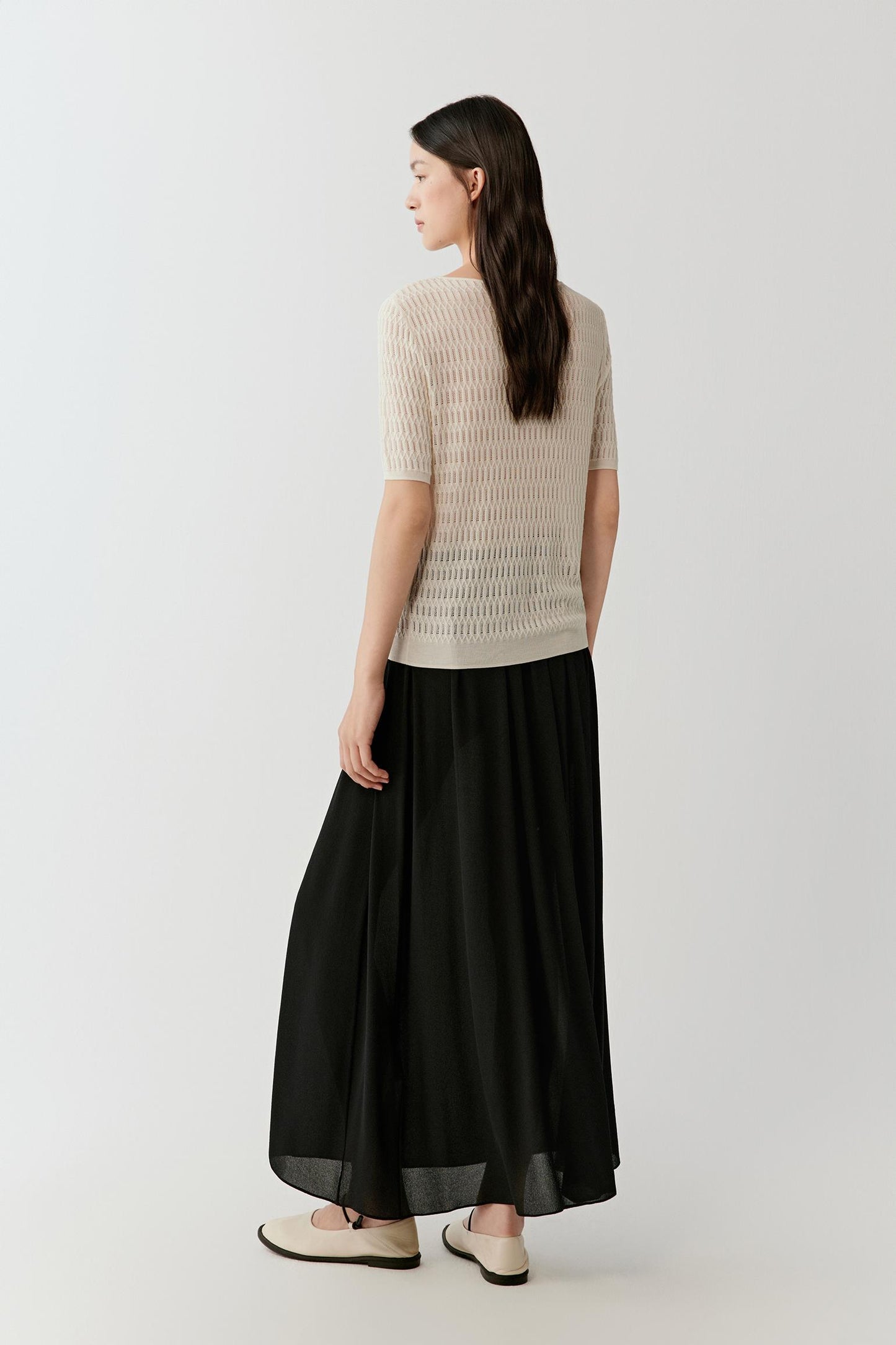Back view emphasizing the soft drape, short sleeve length and airy open-knit construction that creates subtle transparency.