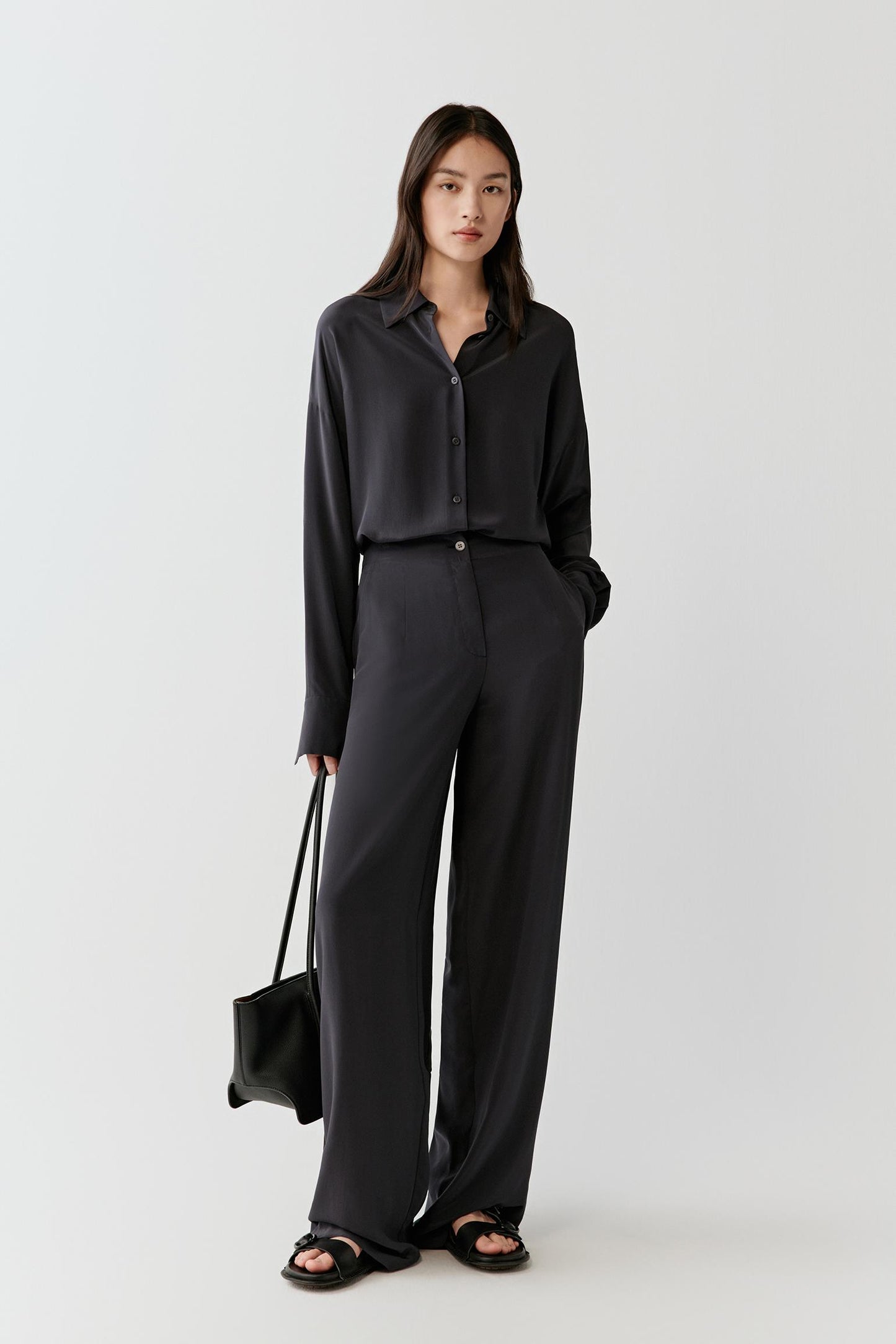 Full-length view of the black silk shirt and trousers, highlighting the fluid silhouette and straight, elongated line of the outfit.