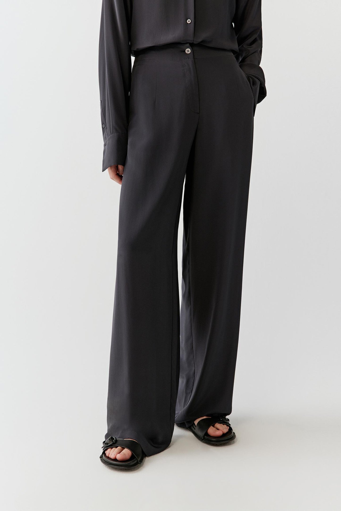 Front view of the black silk trousers, highlighting the clean waistband, straight leg and soft, flowing fabric.
