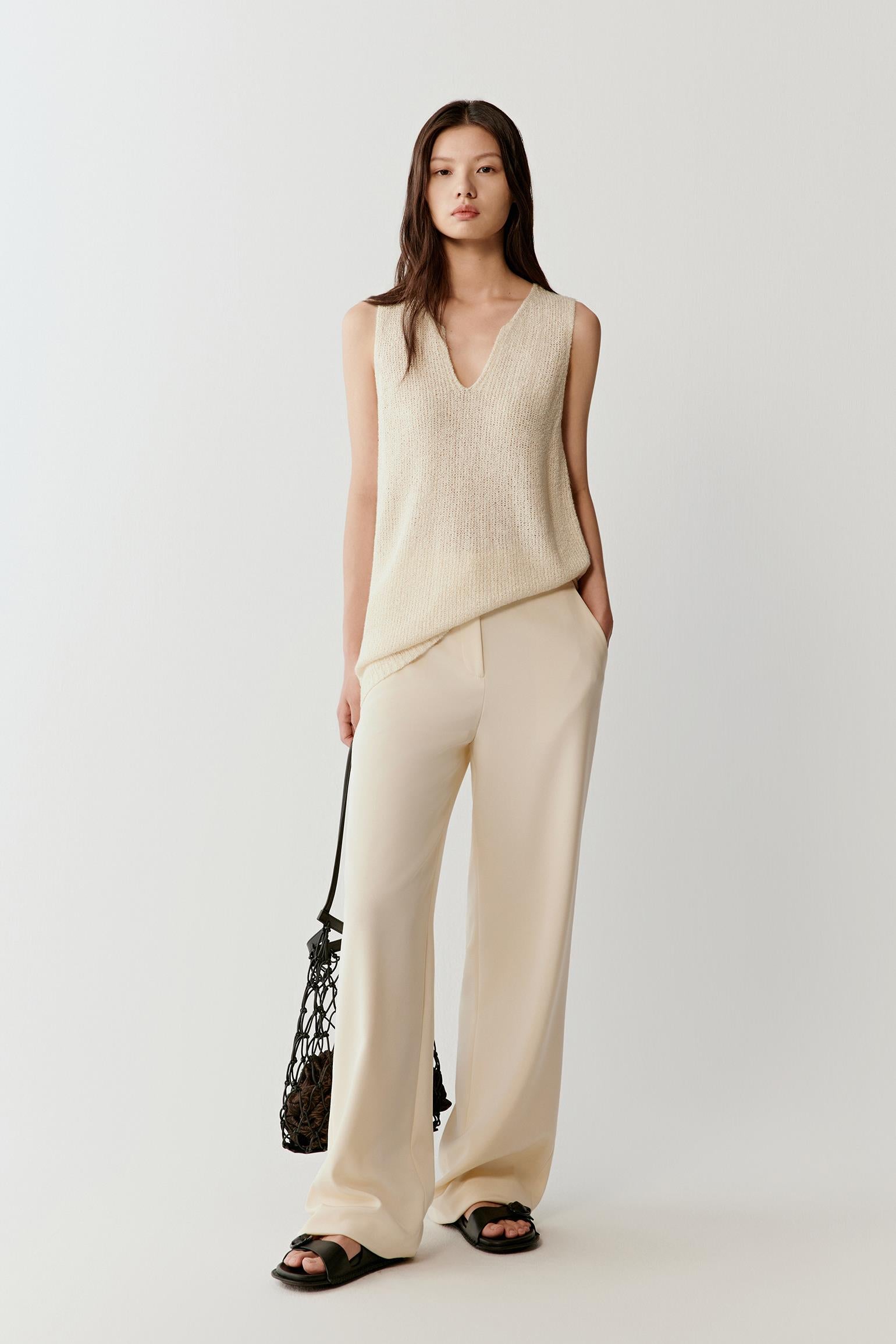 Full-length view of the ivory sleeveless top styled with matching light trousers, highlighting the straight silhouette and lightweight, fluid fall of the knit.