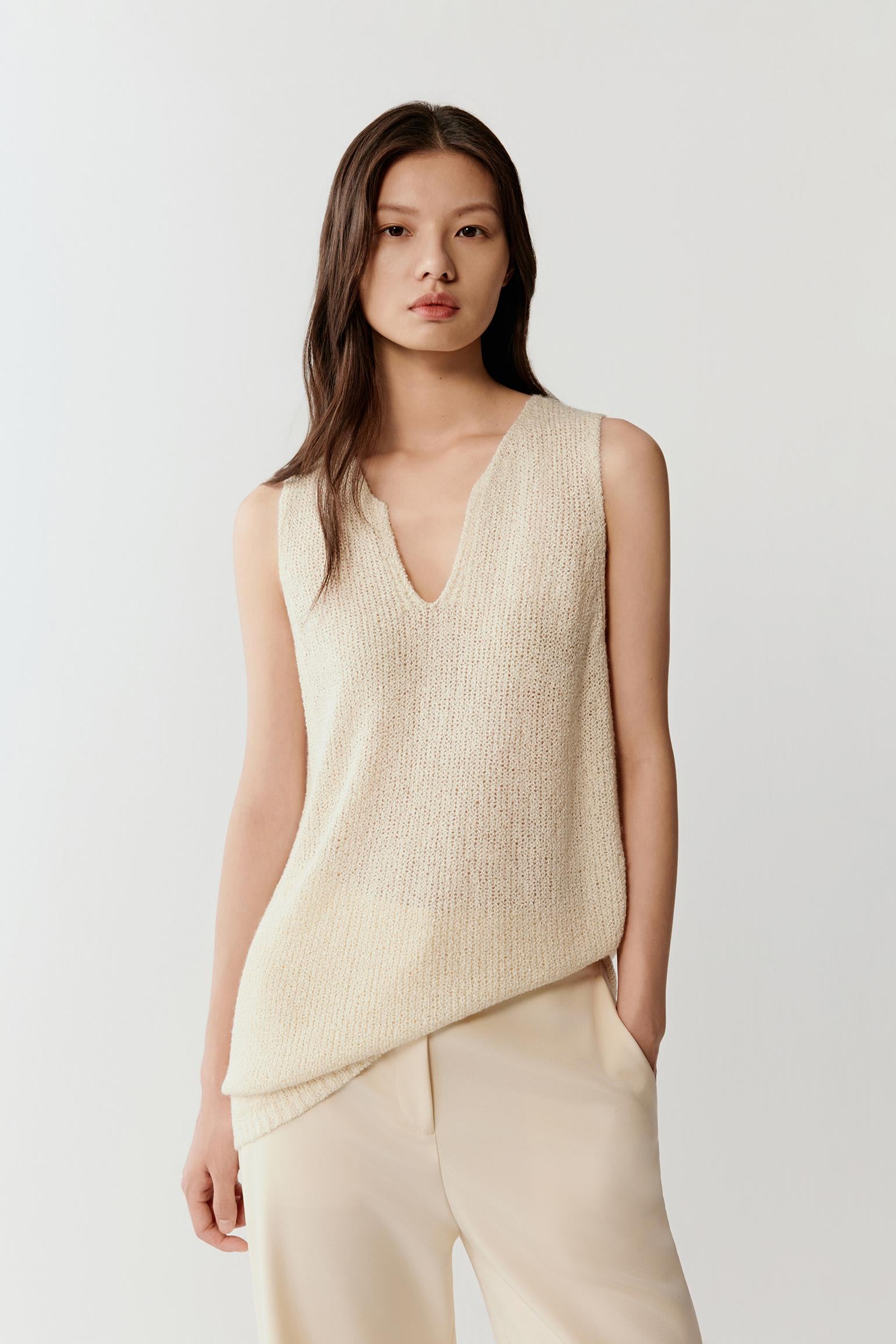 Woman wearing an ivory sleeveless silk knit top with a relaxed, fluid cut and V-neckline, front view showing the soft drape, natural texture and clean shoulder line.
