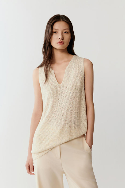 Woman wearing an ivory sleeveless silk knit top with a relaxed, fluid cut and V-neckline, front view showing the soft drape, natural texture and clean shoulder line.