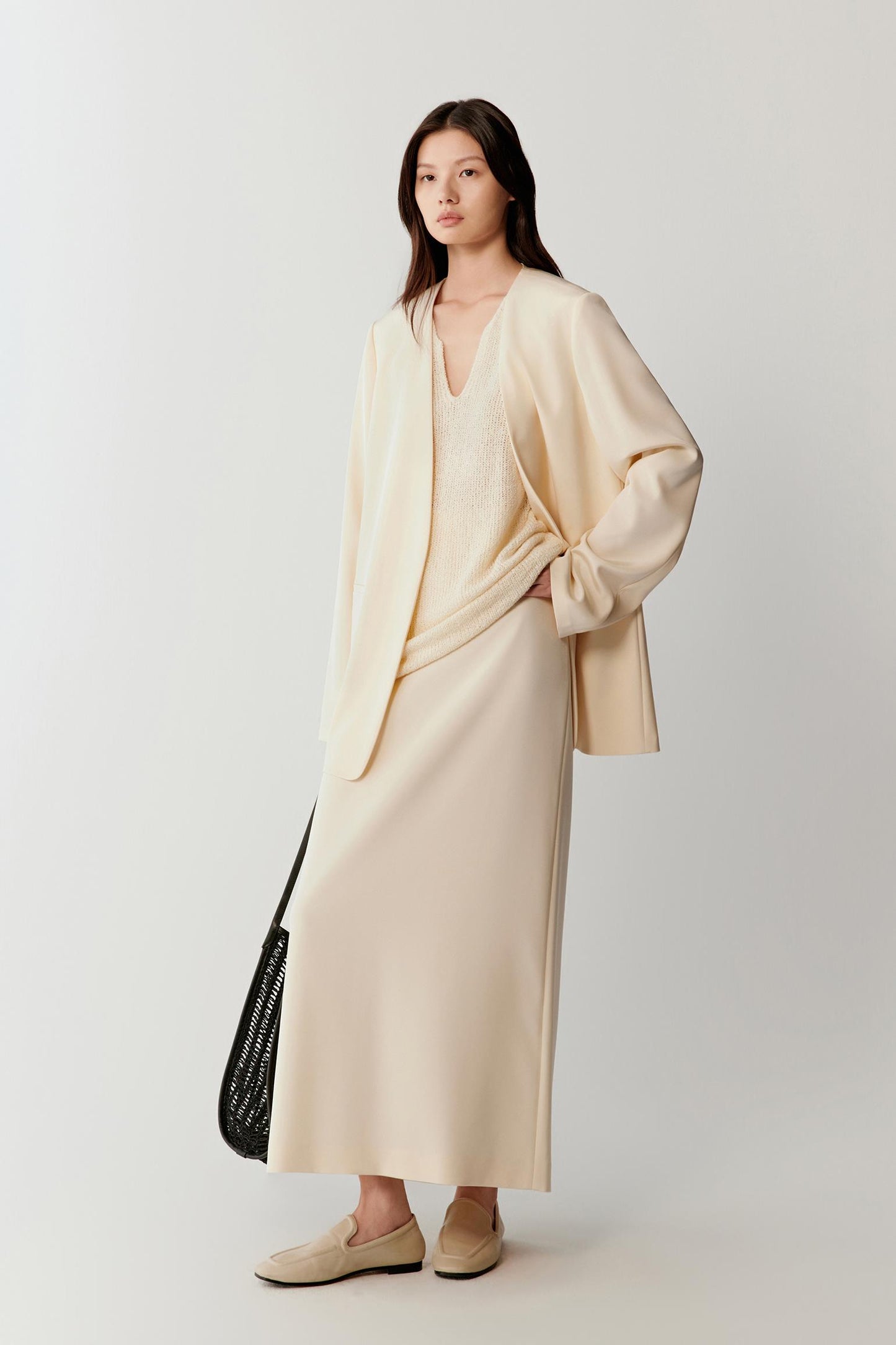 Full-length view of the ivory blazer styled with matching fluid trousers, highlighting the long, straight silhouette and soft movement of the fabric.