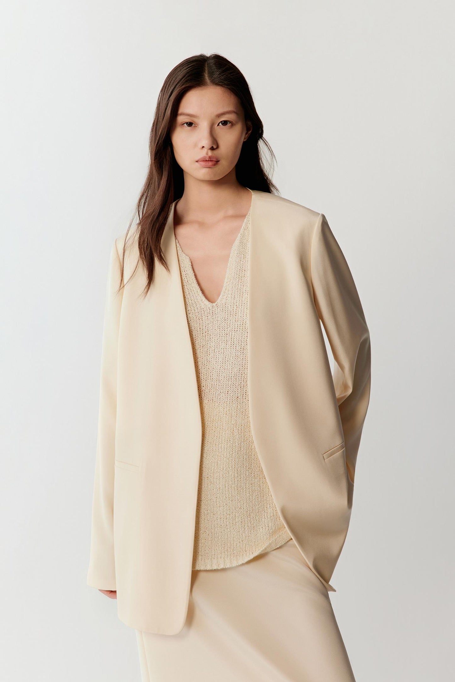 Woman wearing an ivory silk stretch crepe blazer with a straight, relaxed cut and fluid drape, front view showing the clean lines, soft shoulders and lightweight structure.