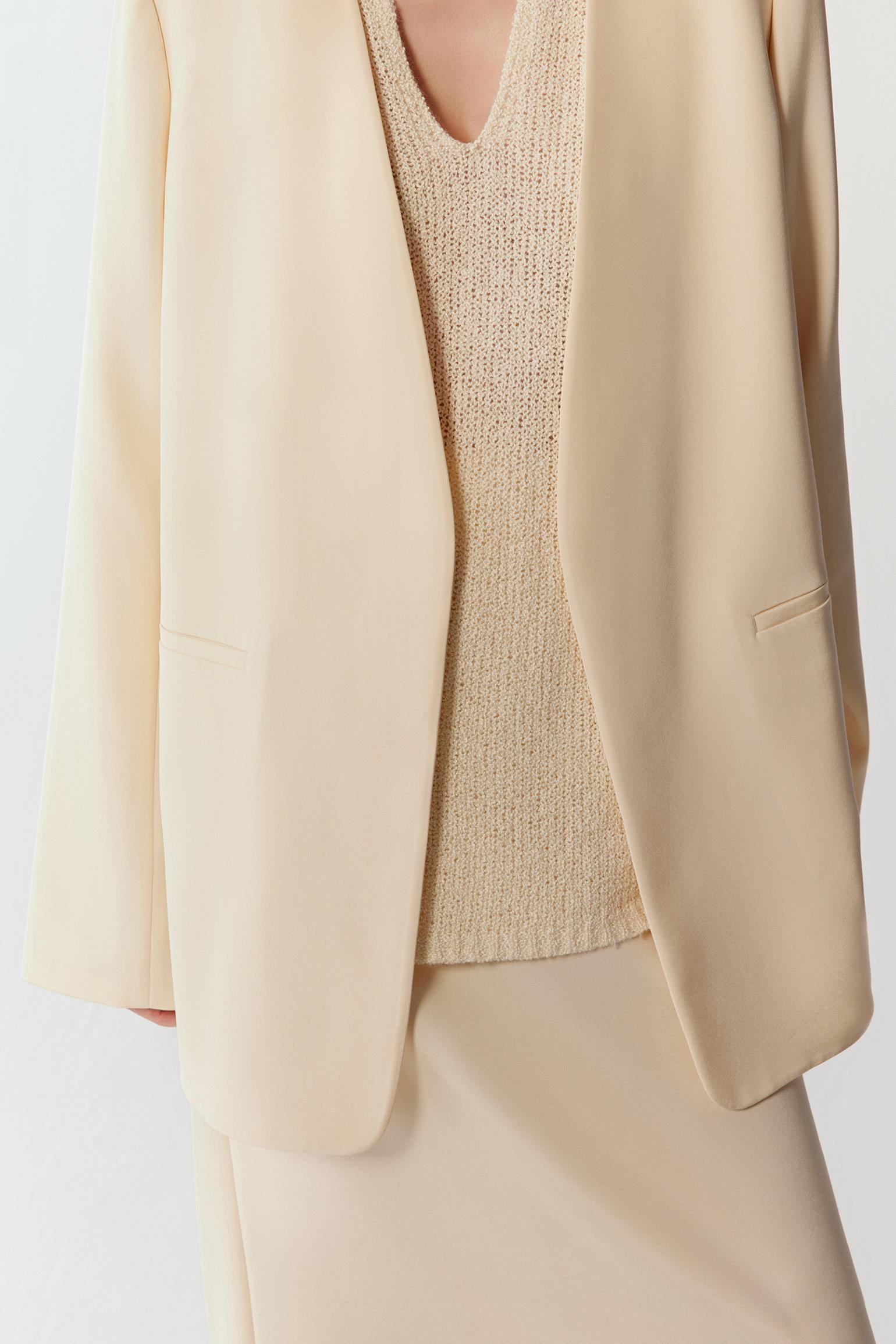 Close-up of the ivory silk crepe fabric and lapel, showing the fine texture, clean finishing and fluid structure.