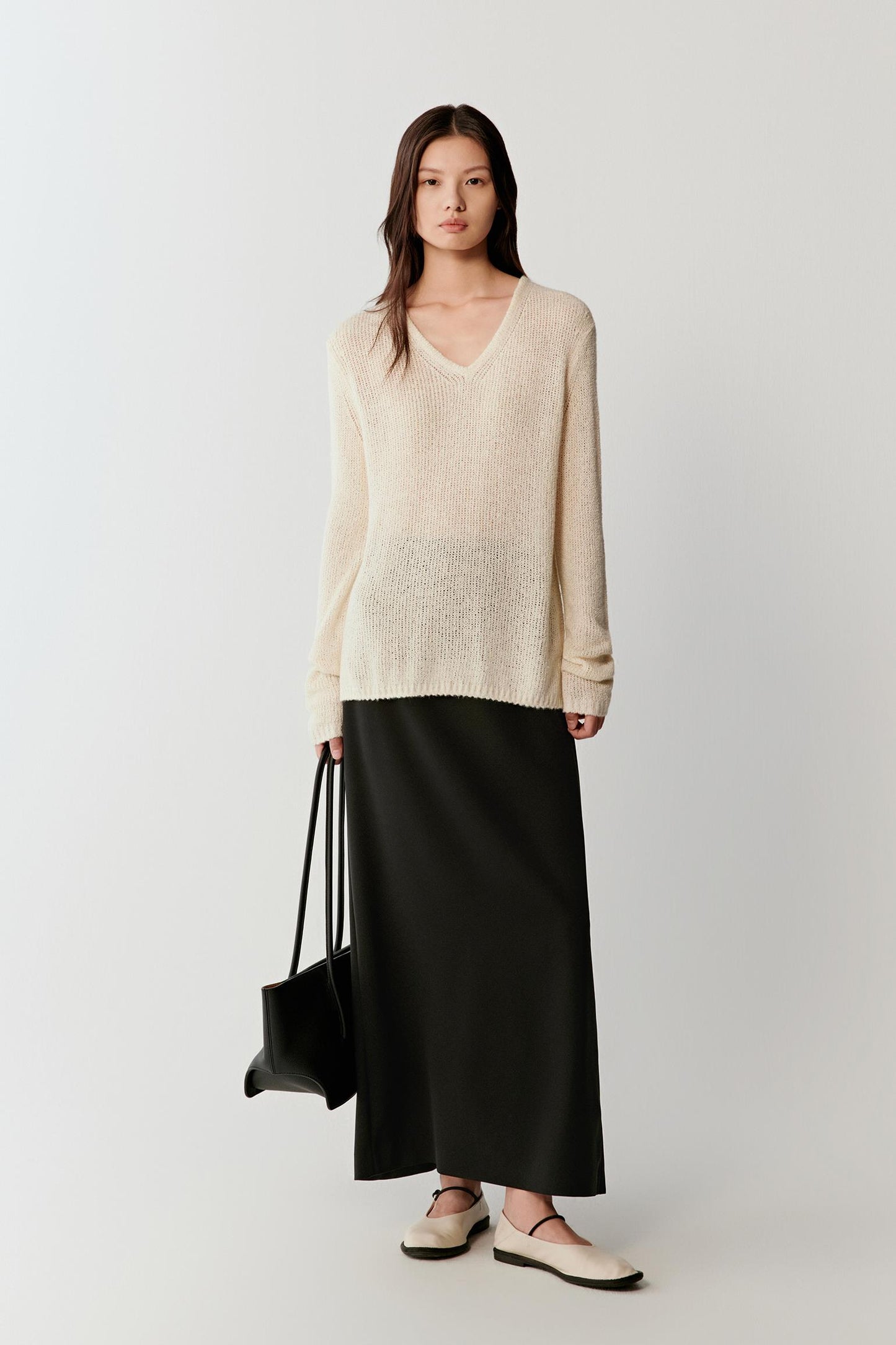 Woman wearing an ivory spun silk knit pullover with a relaxed, slightly loose cut and V-neckline, styled with a long black skirt, full-length view showing the fluid drape and lightweight knit.