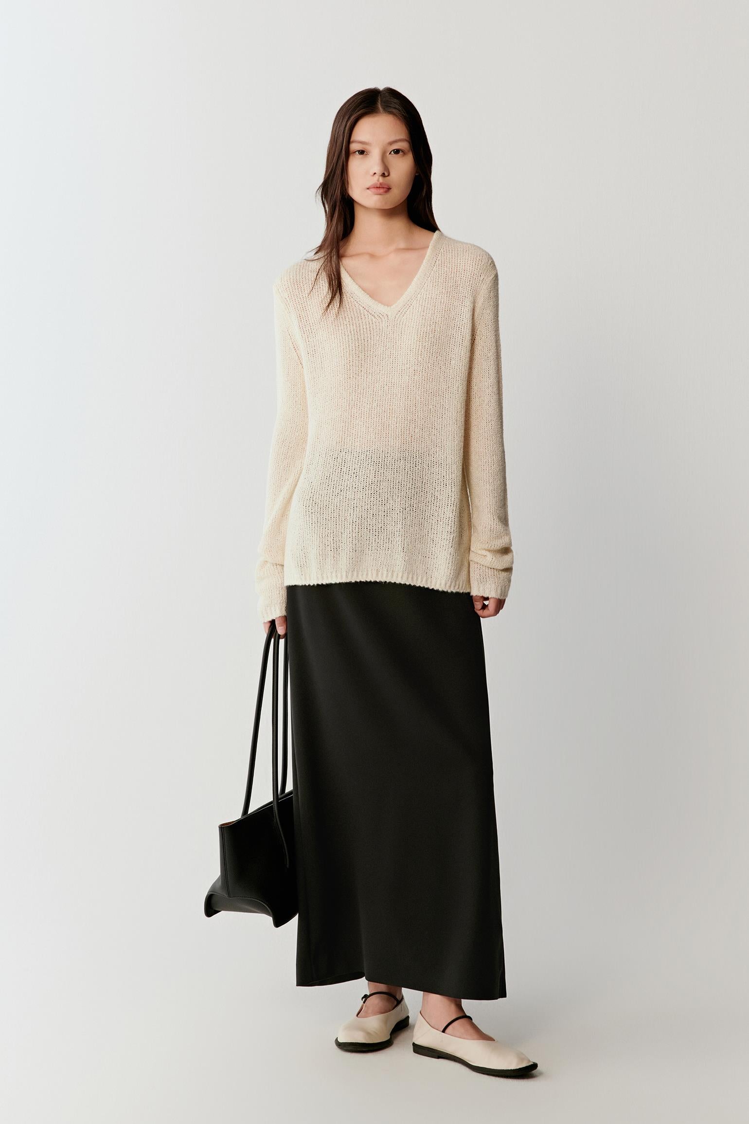 Woman wearing an ivory spun silk knit pullover with a relaxed, slightly loose cut and V-neckline, styled with a long black skirt, full-length view showing the fluid drape and lightweight knit.