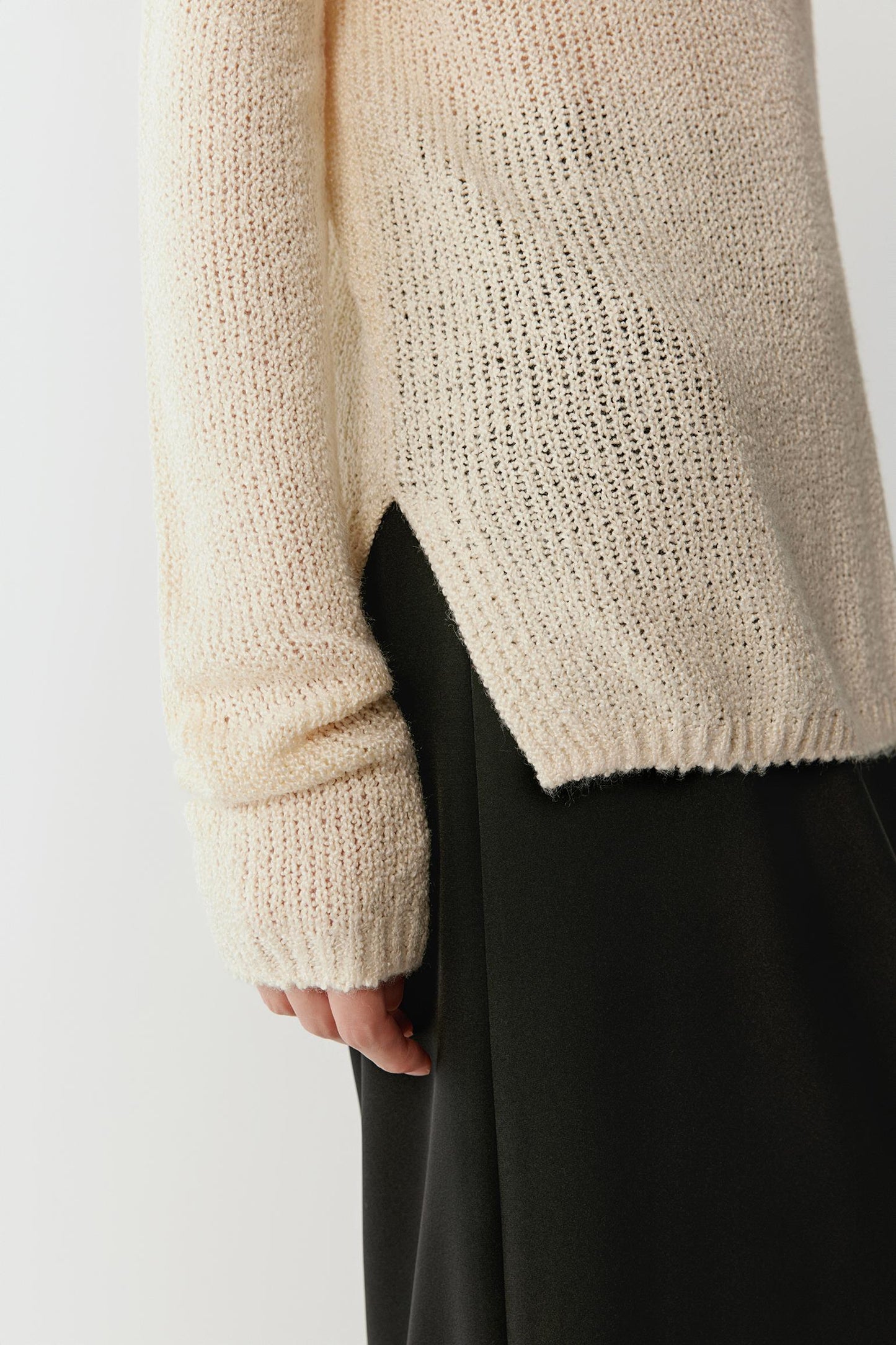 Detail of the sleeve and hem, highlighting the soft finishing and open knit structure.