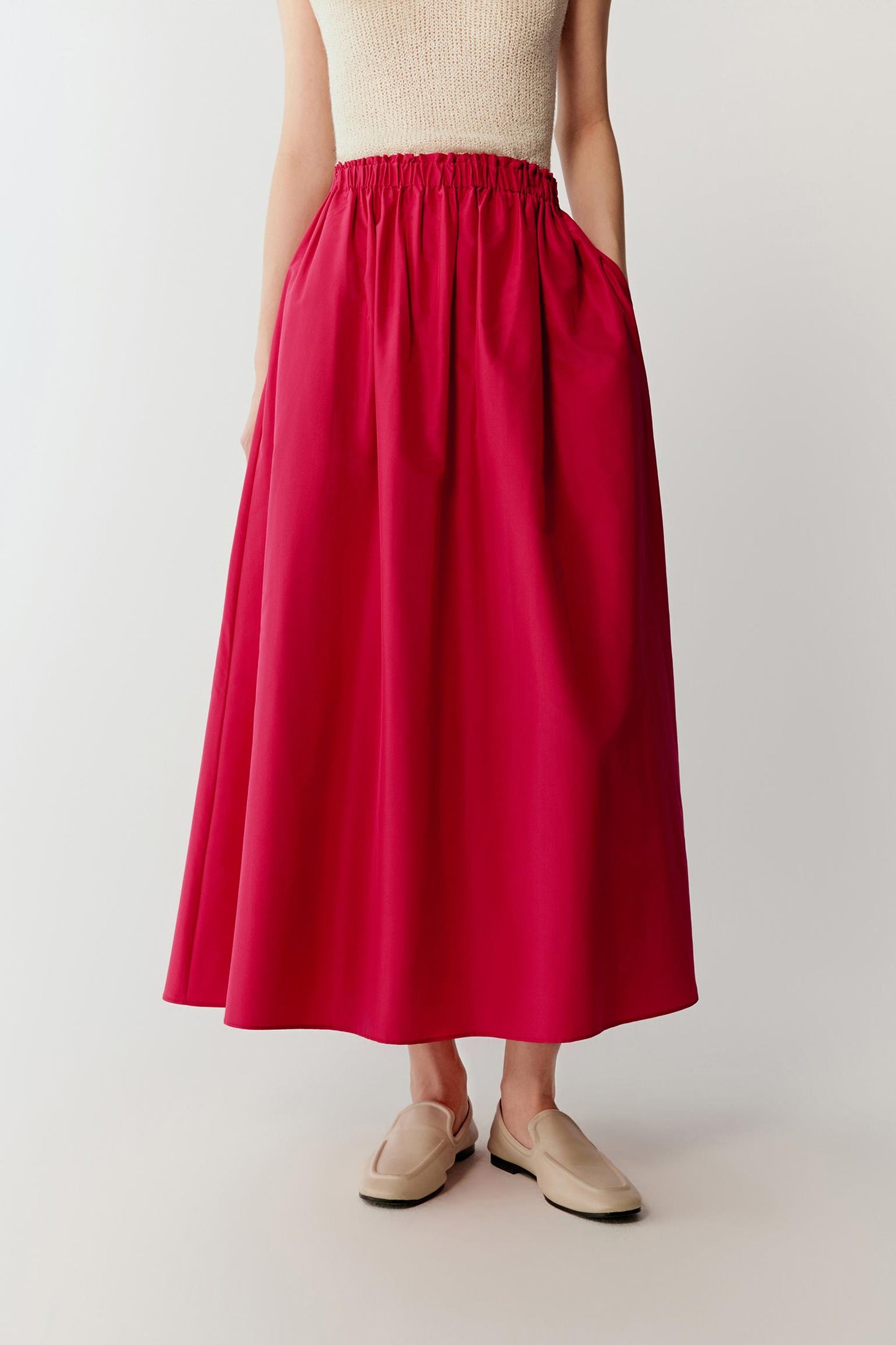 Mid-length front view focusing on the skirt from waist to hem, emphasizing the gathered waistline and the way the fabric expands outward, with the smooth, compact surface reflecting light subtly and enhancing the vivid pink tone
