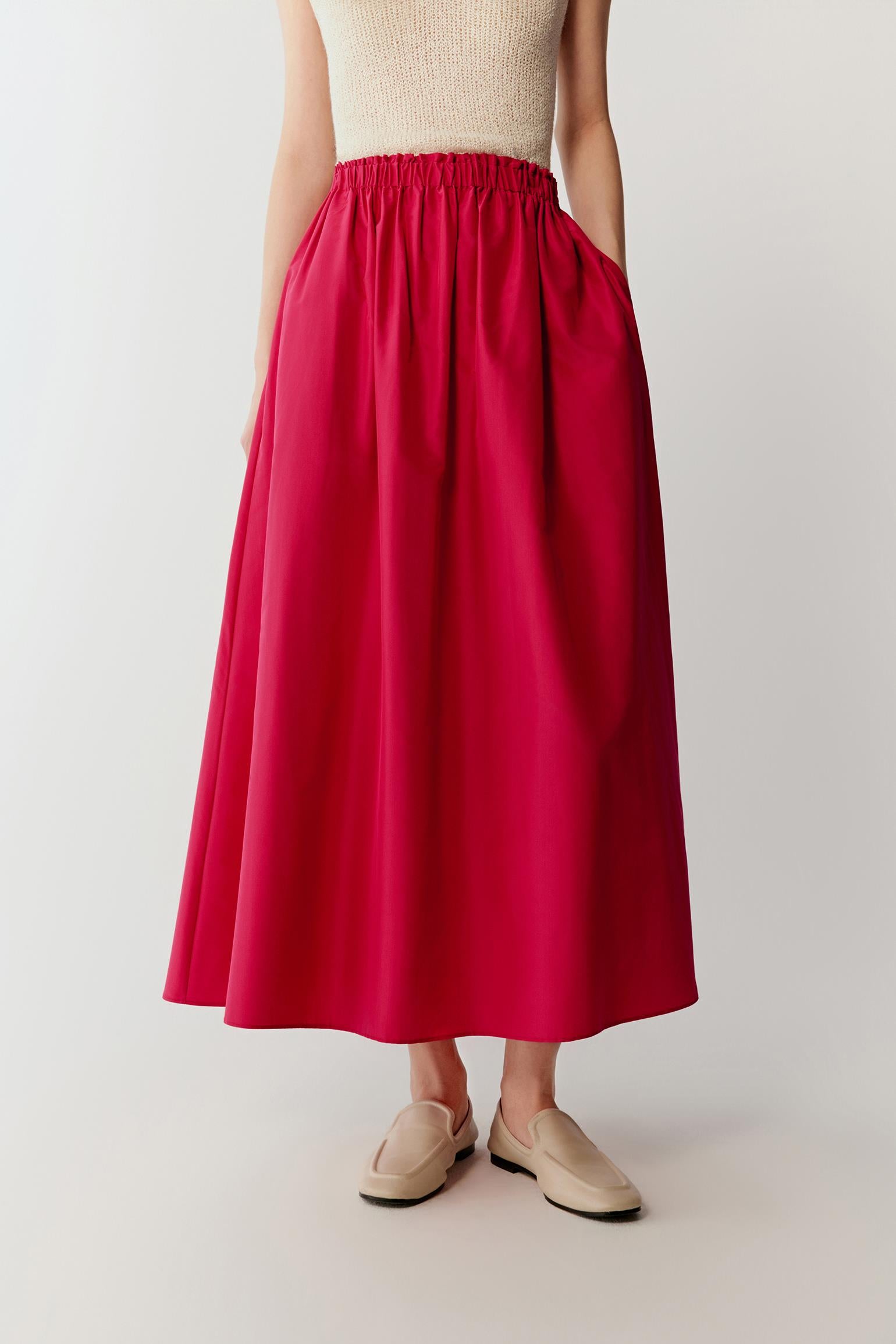 Mid-length front view focusing on the skirt from waist to hem, emphasizing the gathered waistline and the way the fabric expands outward, with the smooth, compact surface reflecting light subtly and enhancing the vivid pink tone