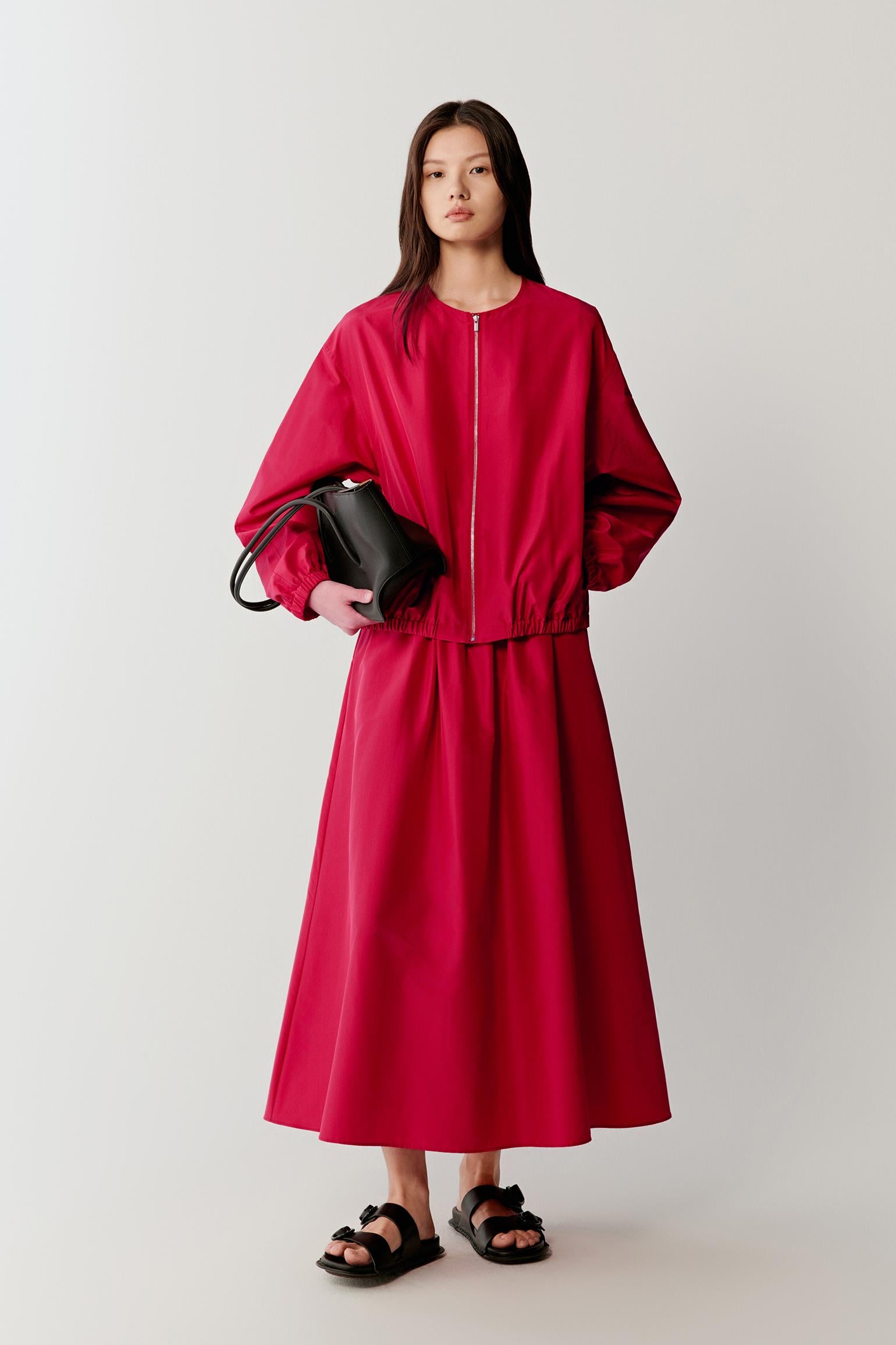 Full-length front view of a woman standing facing forward wearing a bright red silk taffeta long skirt paired with a matching top, highlighting the high-waisted silhouette, gathered construction and full volume, with the fabric holding a structured shape while maintaining fluid movement