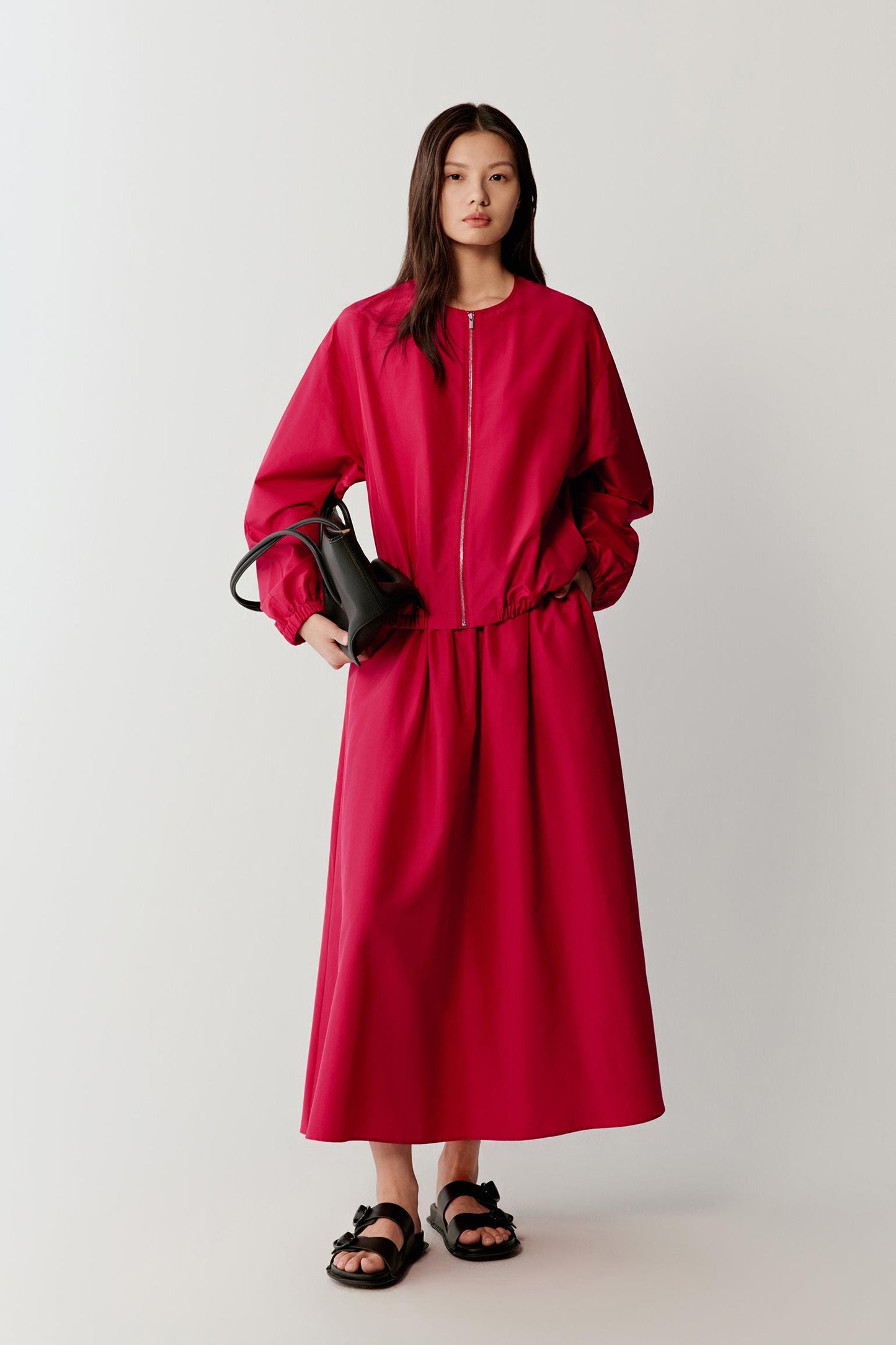 Full-length front view showing the overall silhouette, emphasizing the rounded neckline, front zip closure and generous volume, with the fabric holding its shape while allowing fluid movement, and the bright pink tone appearing vivid and uniform