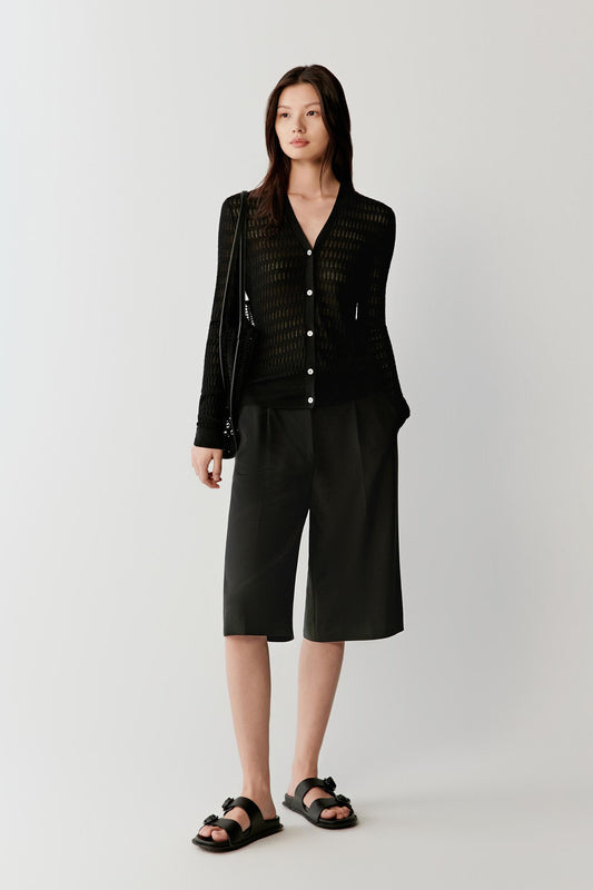 Woman wearing a black silk and linen blend cardigan with a fitted cut and V-neckline, styled with matching cropped trousers, full-length view showing the buttoned front and fluid knit drape.